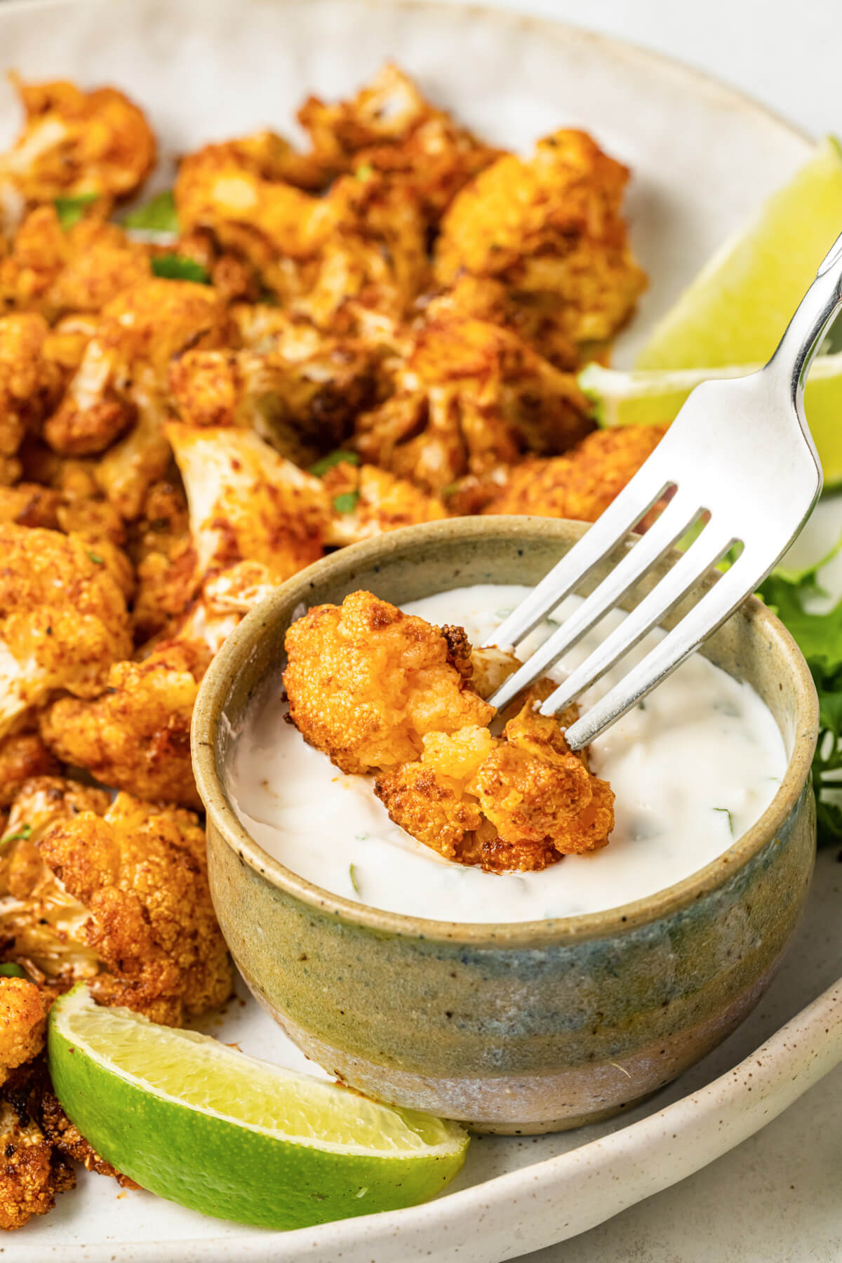 A fork dips a vibrant piece of roasted curried air fryer cauliflower into a creamy dip. 