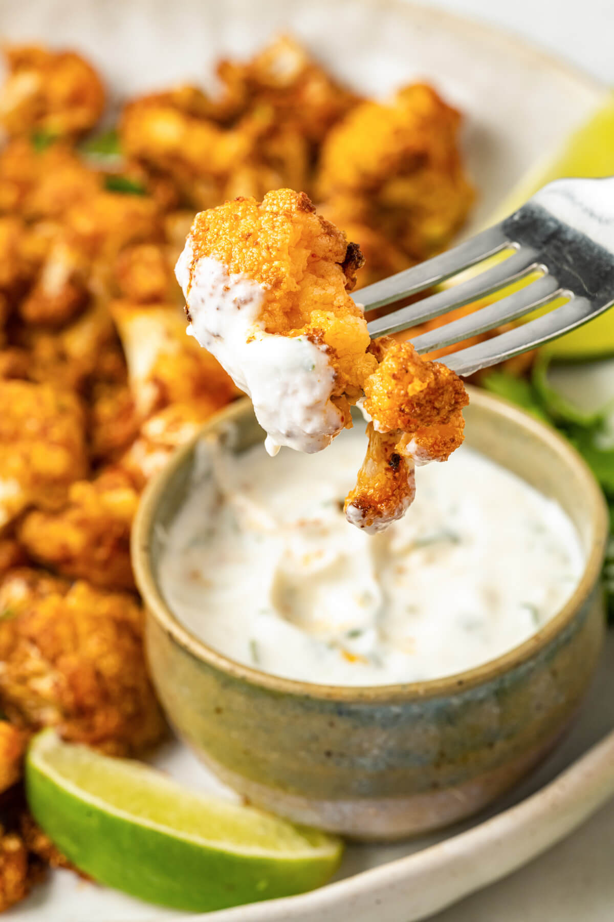 A fork holding a piece of air fried cauliflower with dip over a bowl of yogurt dip.