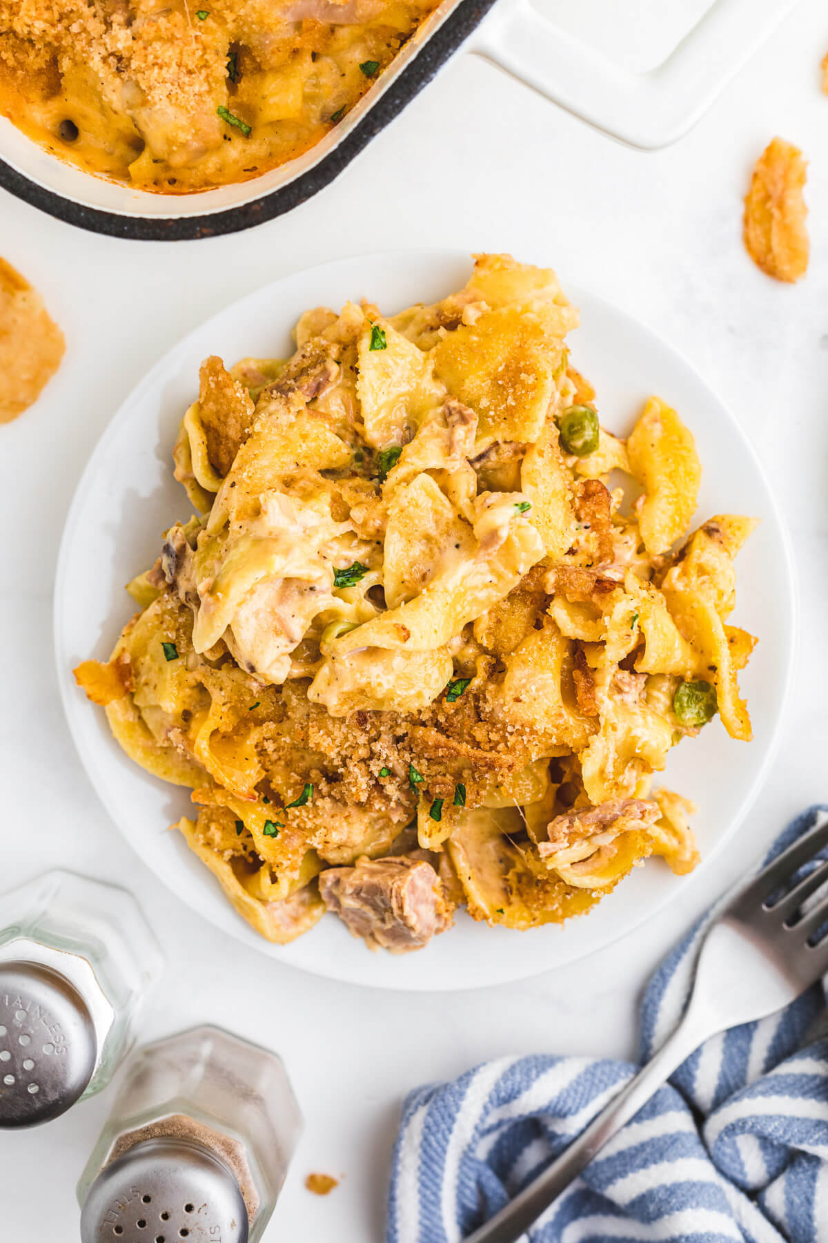 A white dinner plate full of flaked tuna and noodles in a creamy sauce topped with crispy golden bread crumbs.