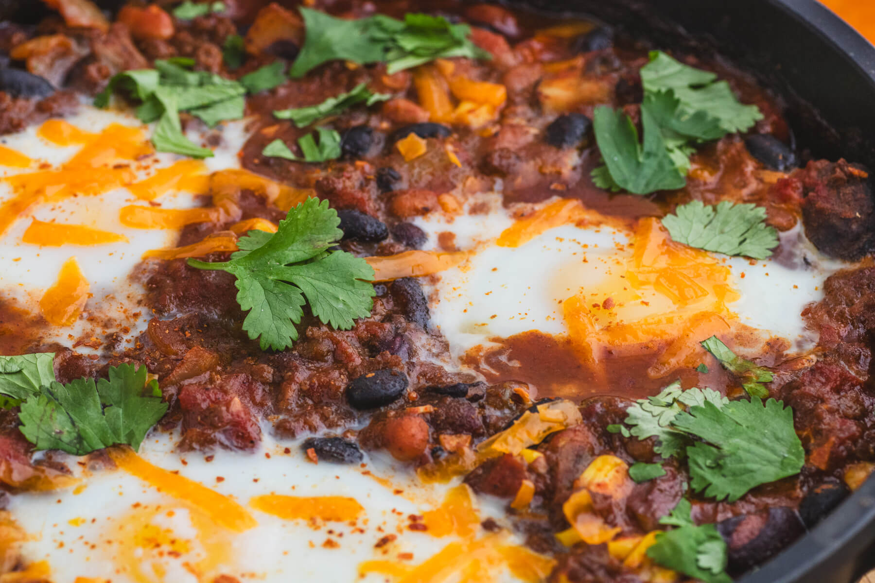 Close up image of baked chili and eggs in a cast iron pan.
