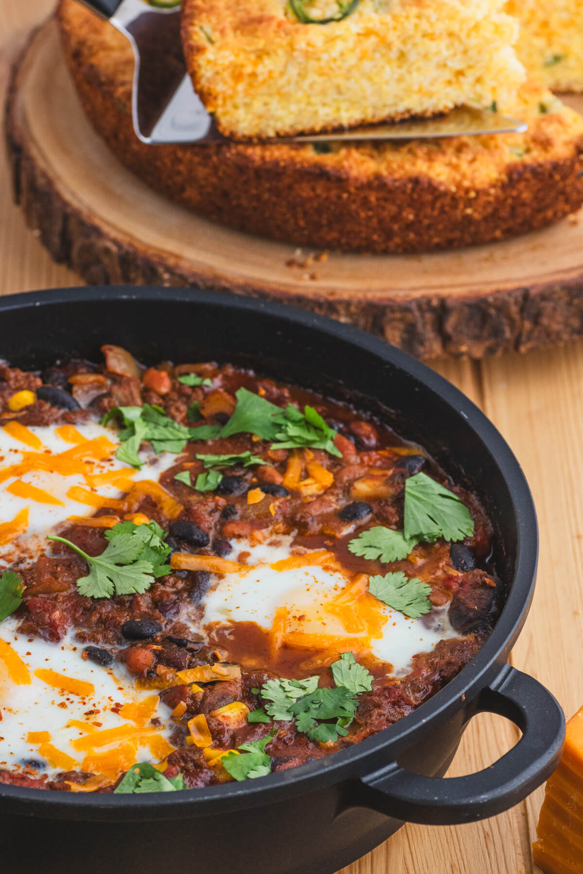 A cast iron skillet full of baked chili and eggs beside jalapeno cheddar cornbread.
