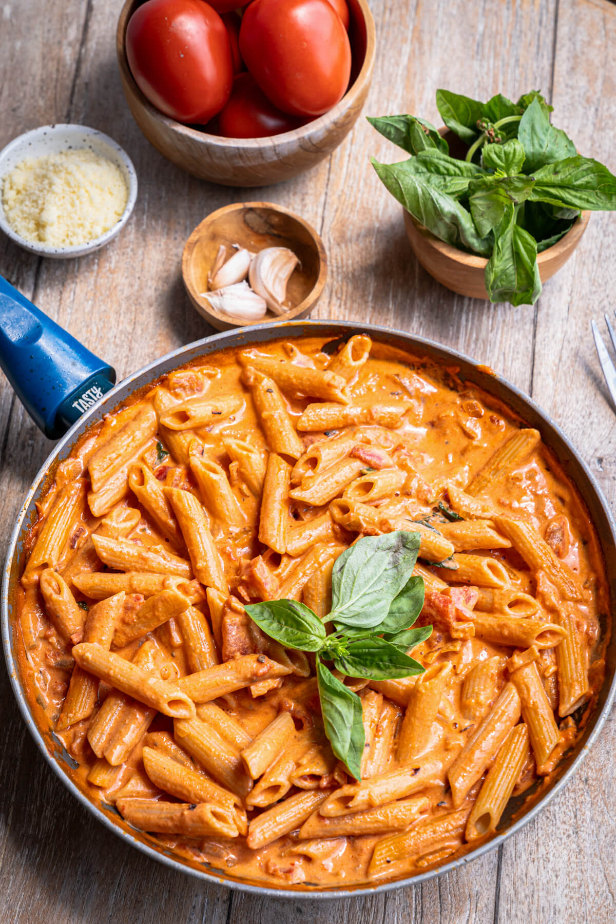 A skillet filled with penne pasta in Rosé sauce garnished with fresh basil leaves.