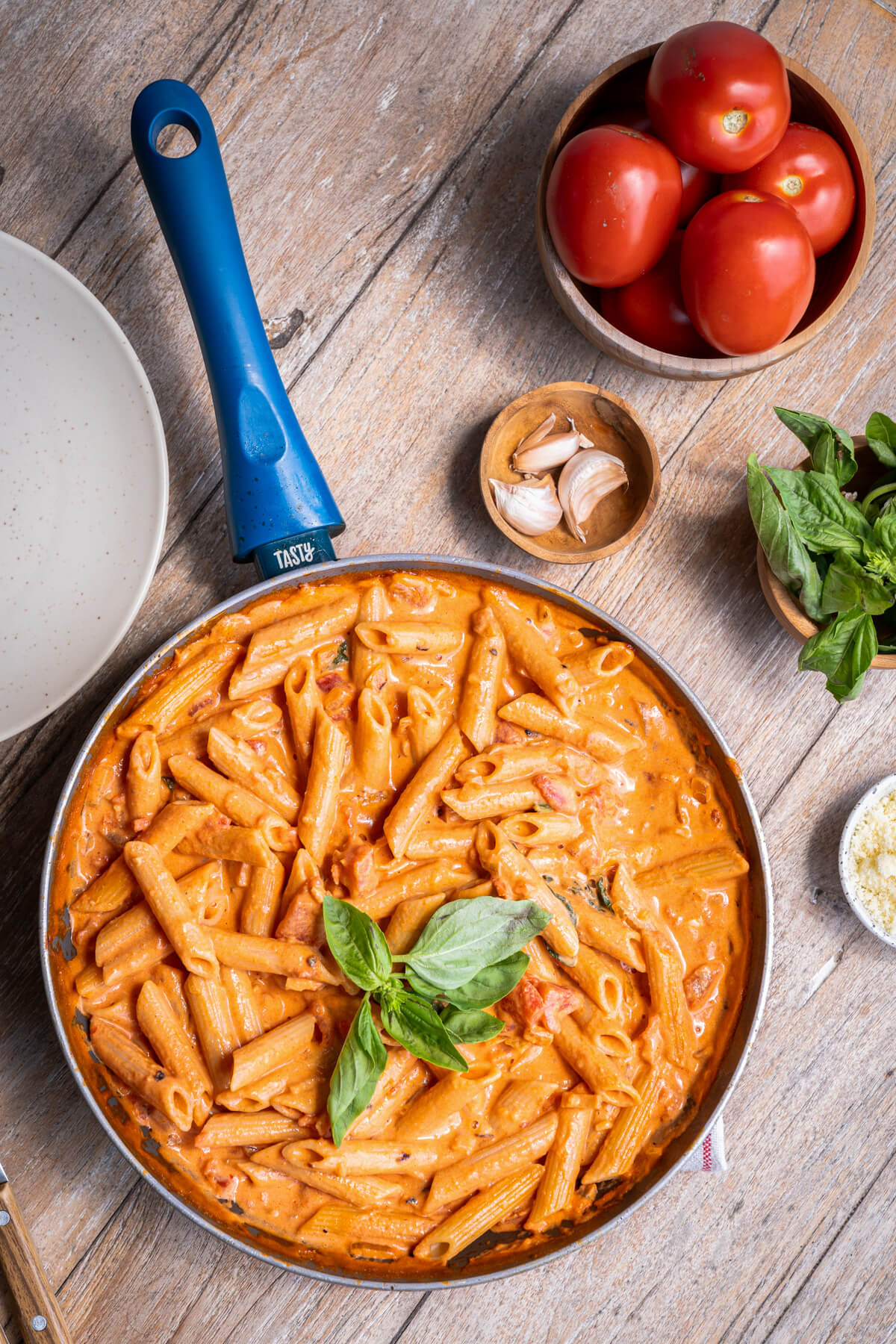 A skillet filled with penne pasta in Rosé sauce garnished with fresh basil leaves.