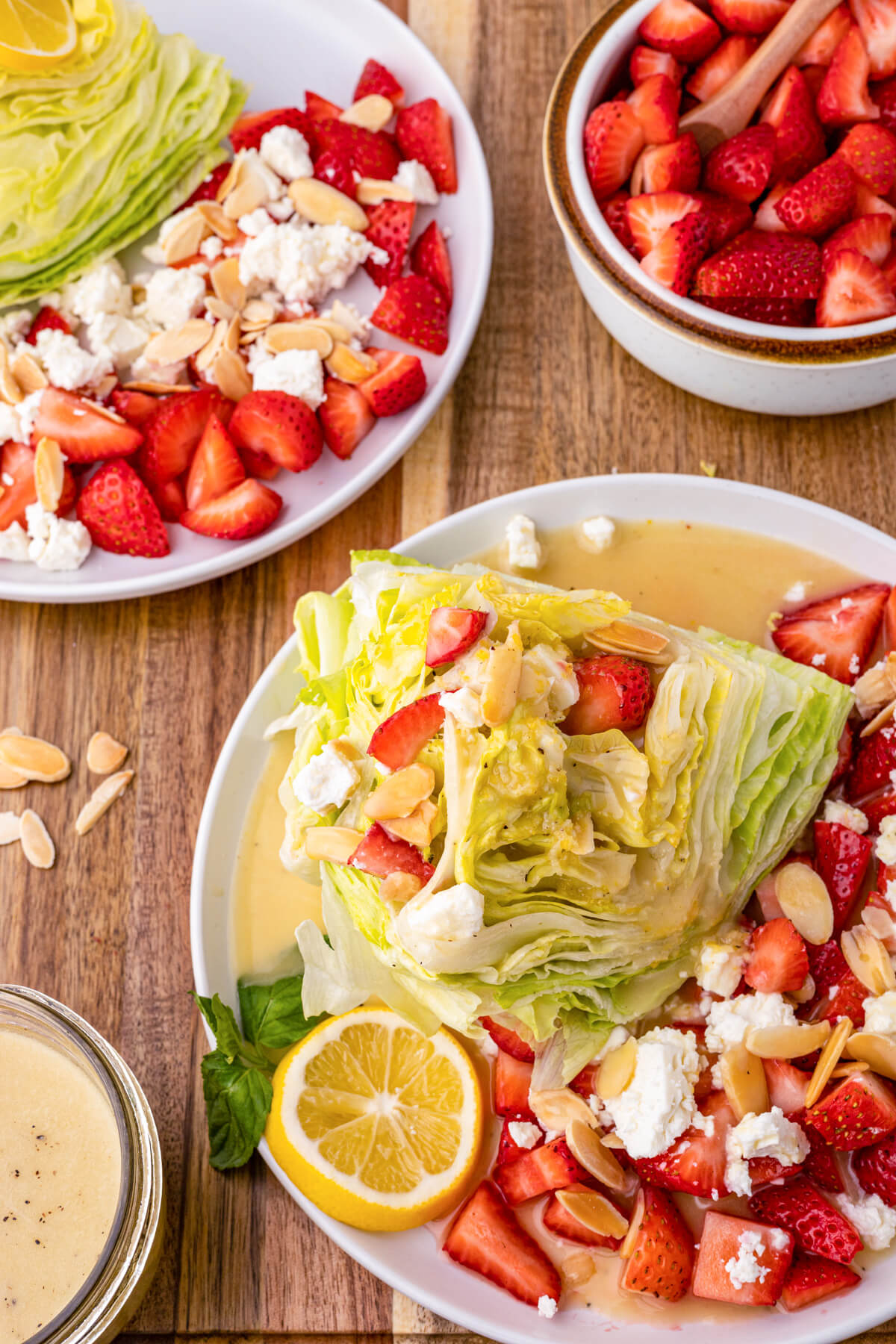 Two strawberry Feta Wedge Salads on white plates on a wooden table.
