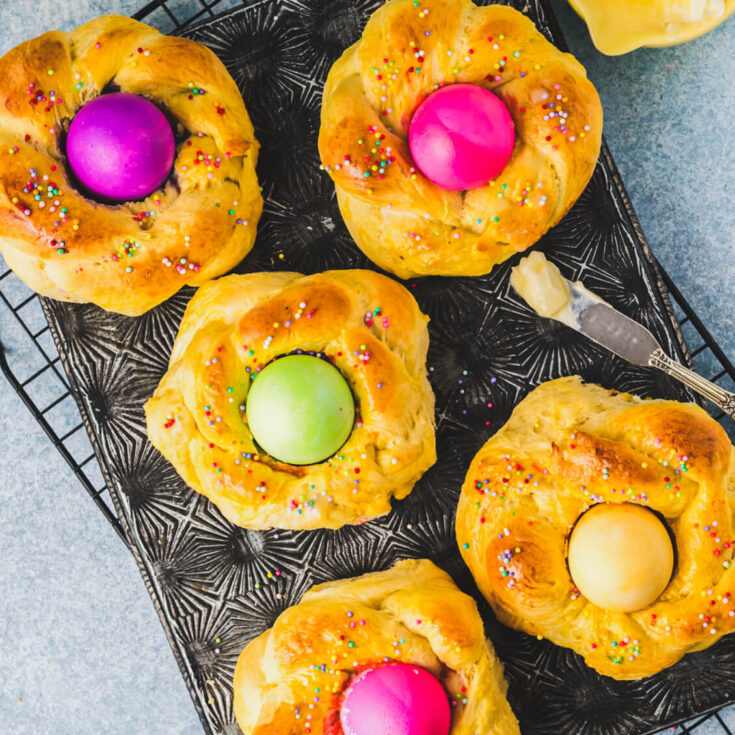 A group of golden baked Italian Easter Bread filled with brightly coloured Easter eggs on a baking sheet.