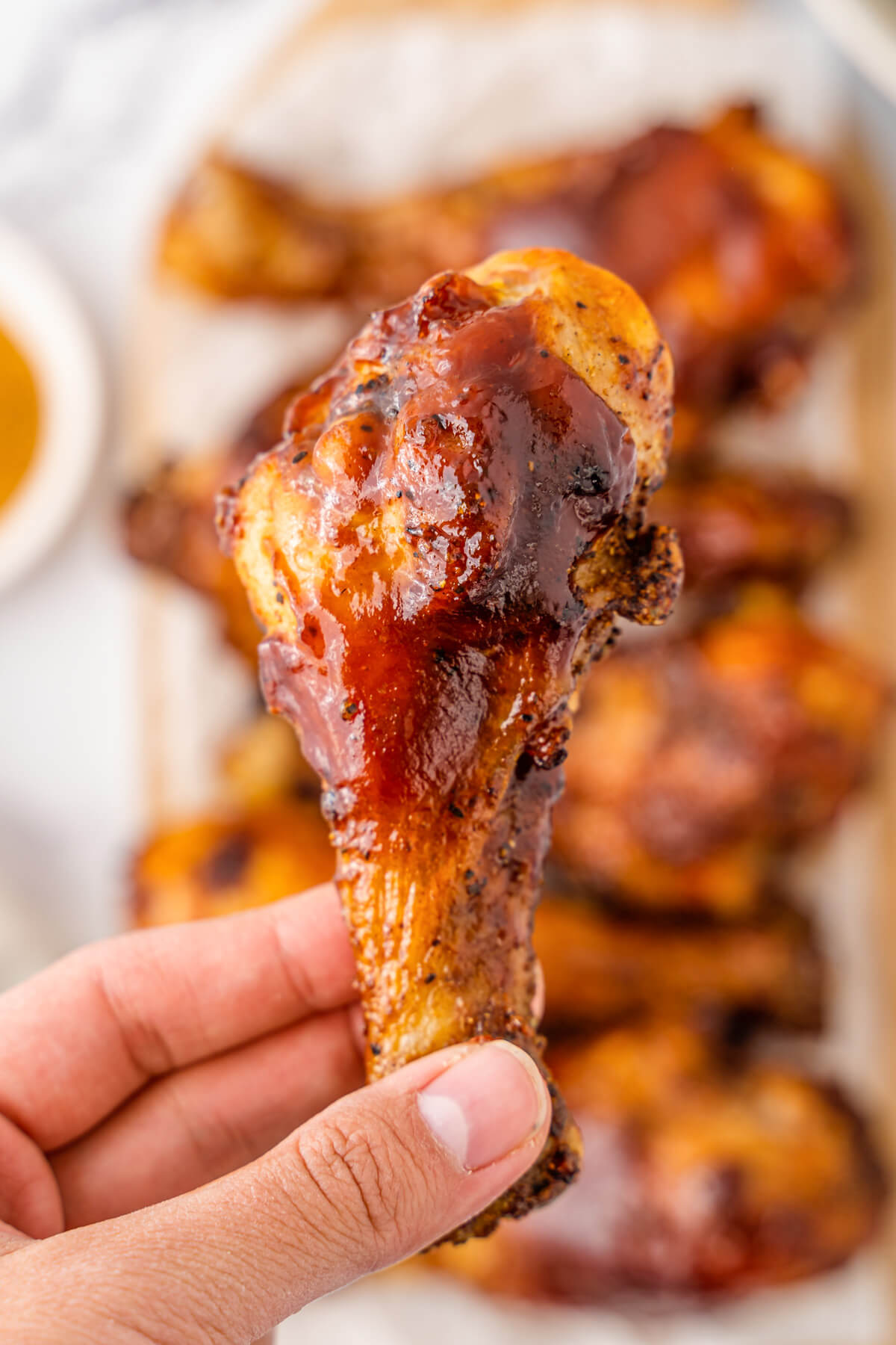 A hand holds a chicken leg coated in barbecue sauce.