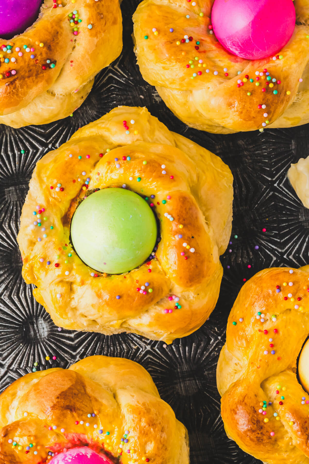 A group of golden baked Italian Easter Bread filled with brightly coloured Easter eggs on a baking sheet.