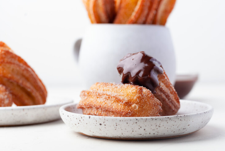 Three golden fried churros on a plate with one that has been dipped in warm chocolate.