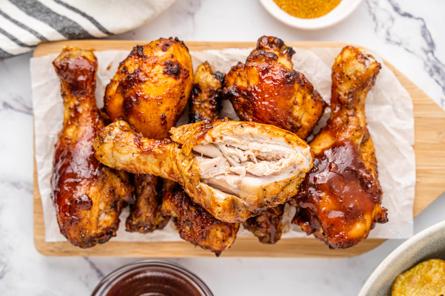 Crispy cooked chicken drumsticks coated in barbecue sauce with the one on top cut open to show the juicy interior.