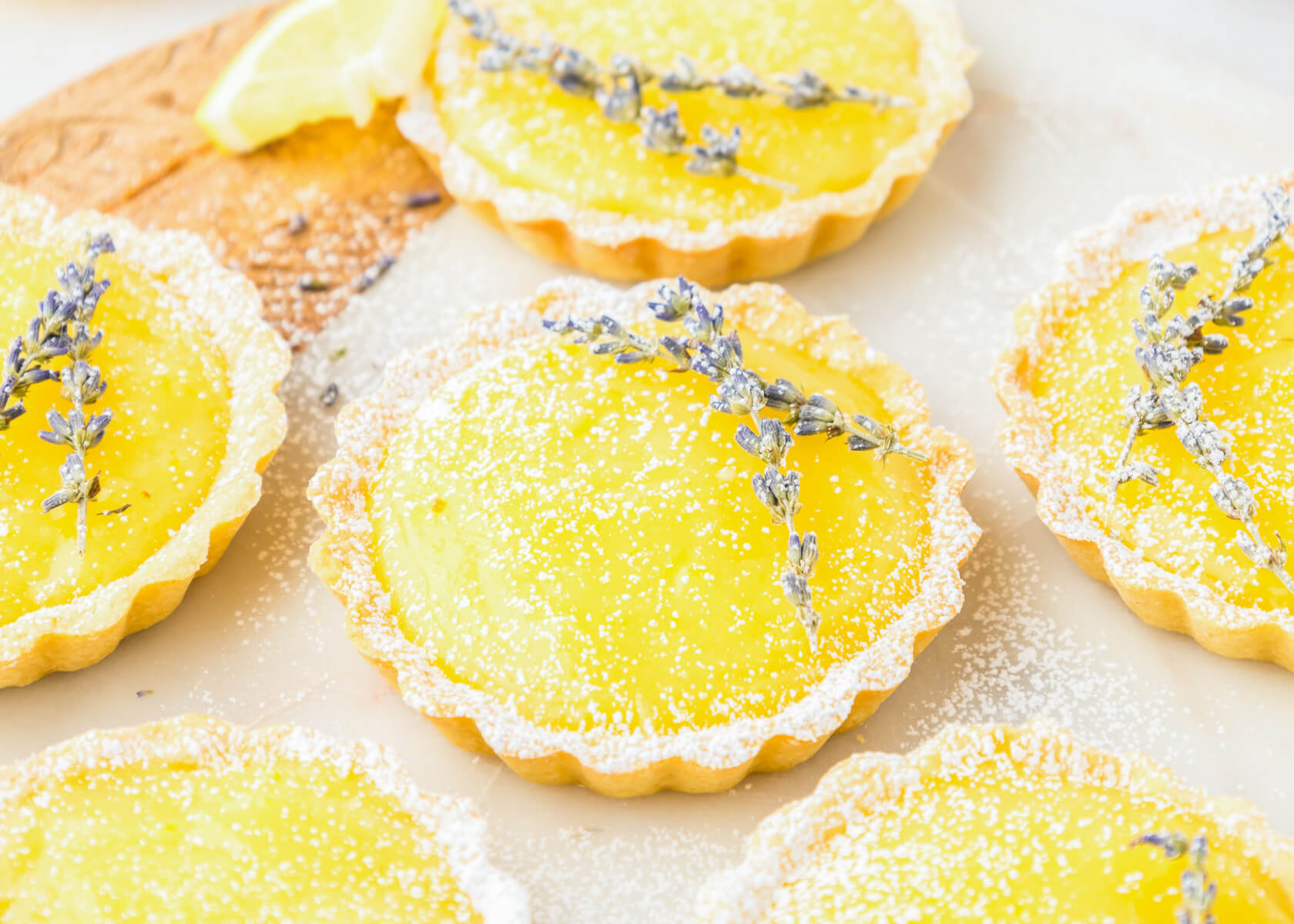 A group of six lemon curd tarts each garnished with two sprigs of purple lavender and dusted with powdered sugar.