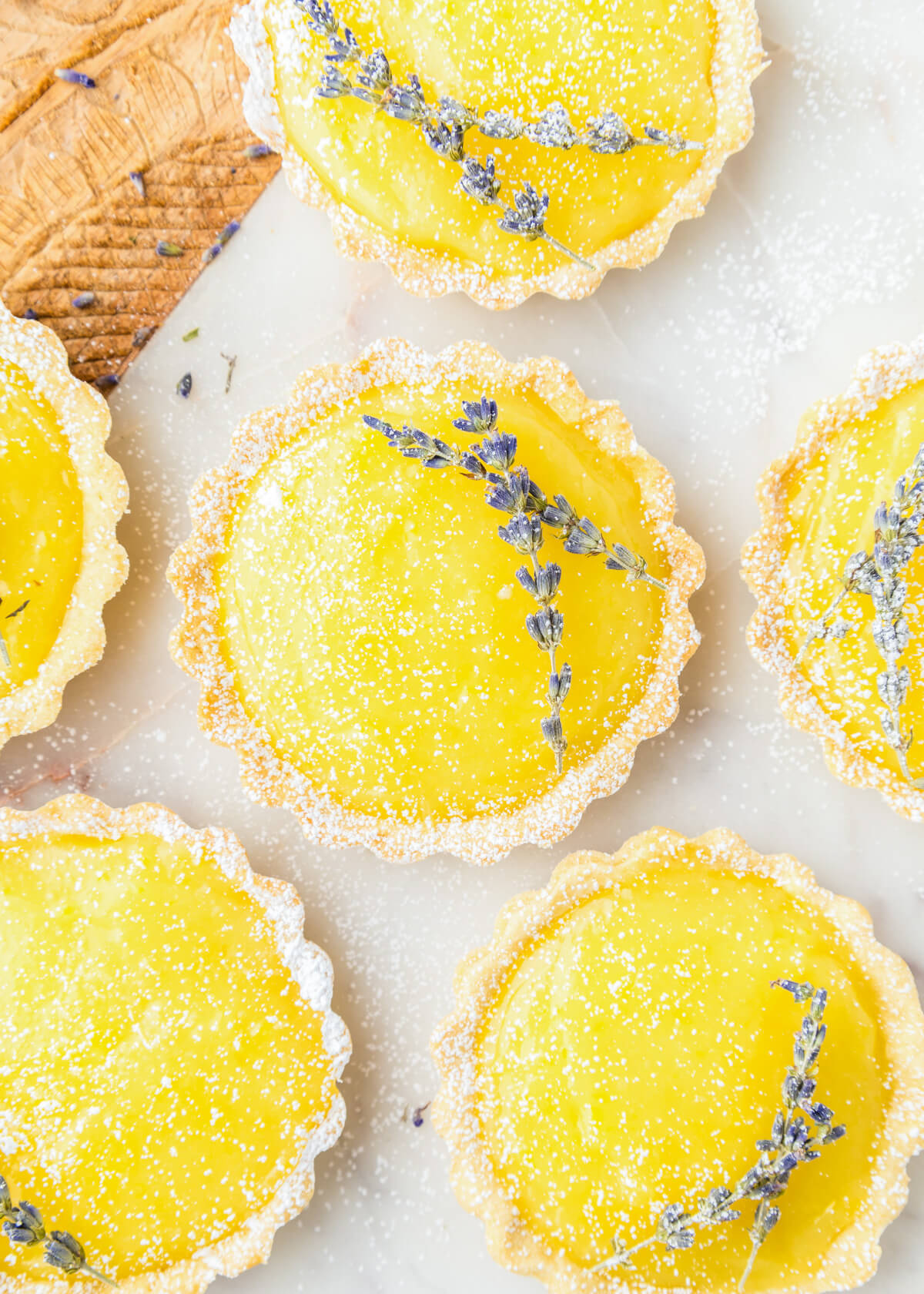 A group of six lemon curd tarts each garnished with two sprigs of purple lavender and dusted with powdered sugar.