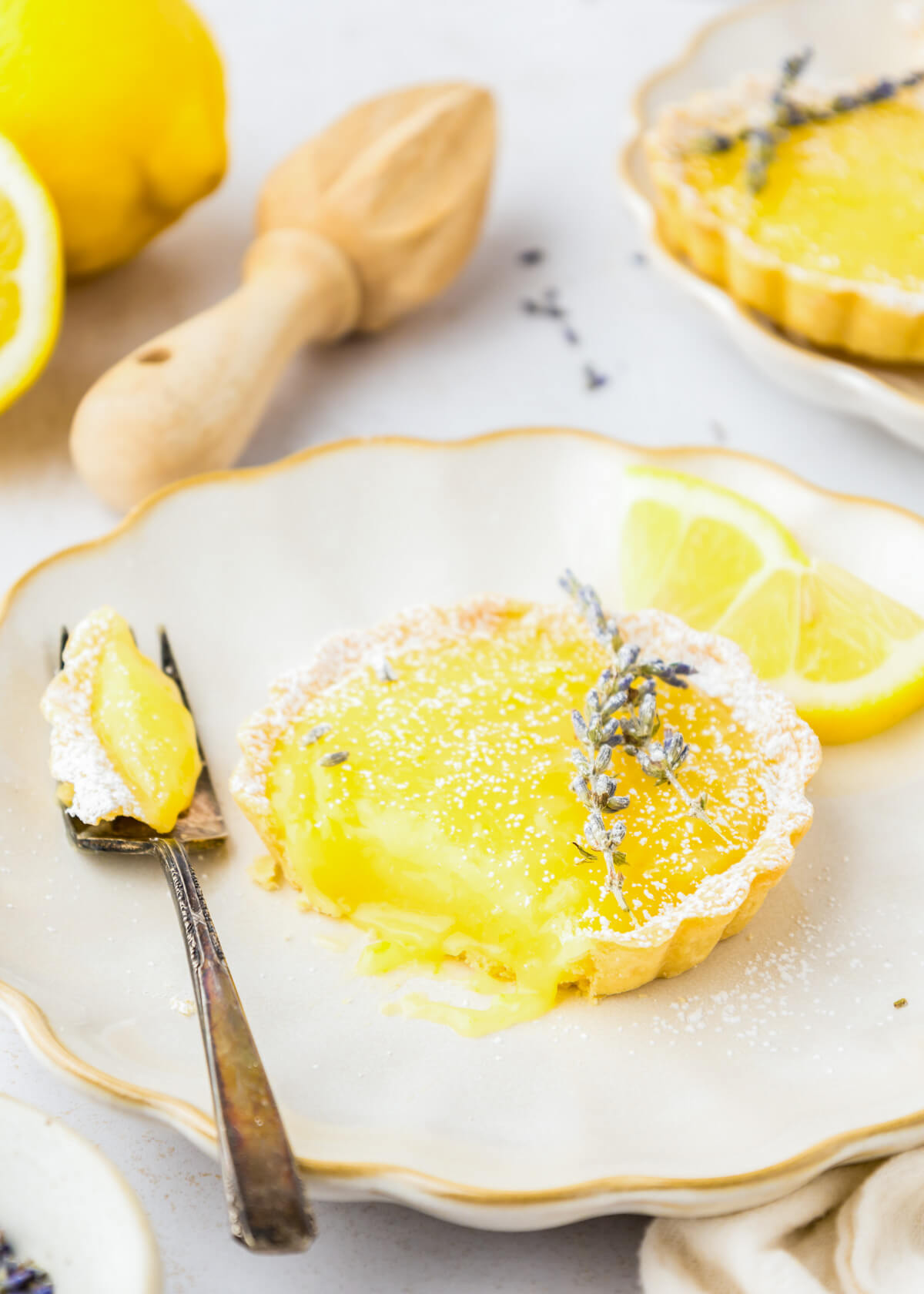One lemon curd tart on a white dessert plate with a fork containing a bite of the same tart. 