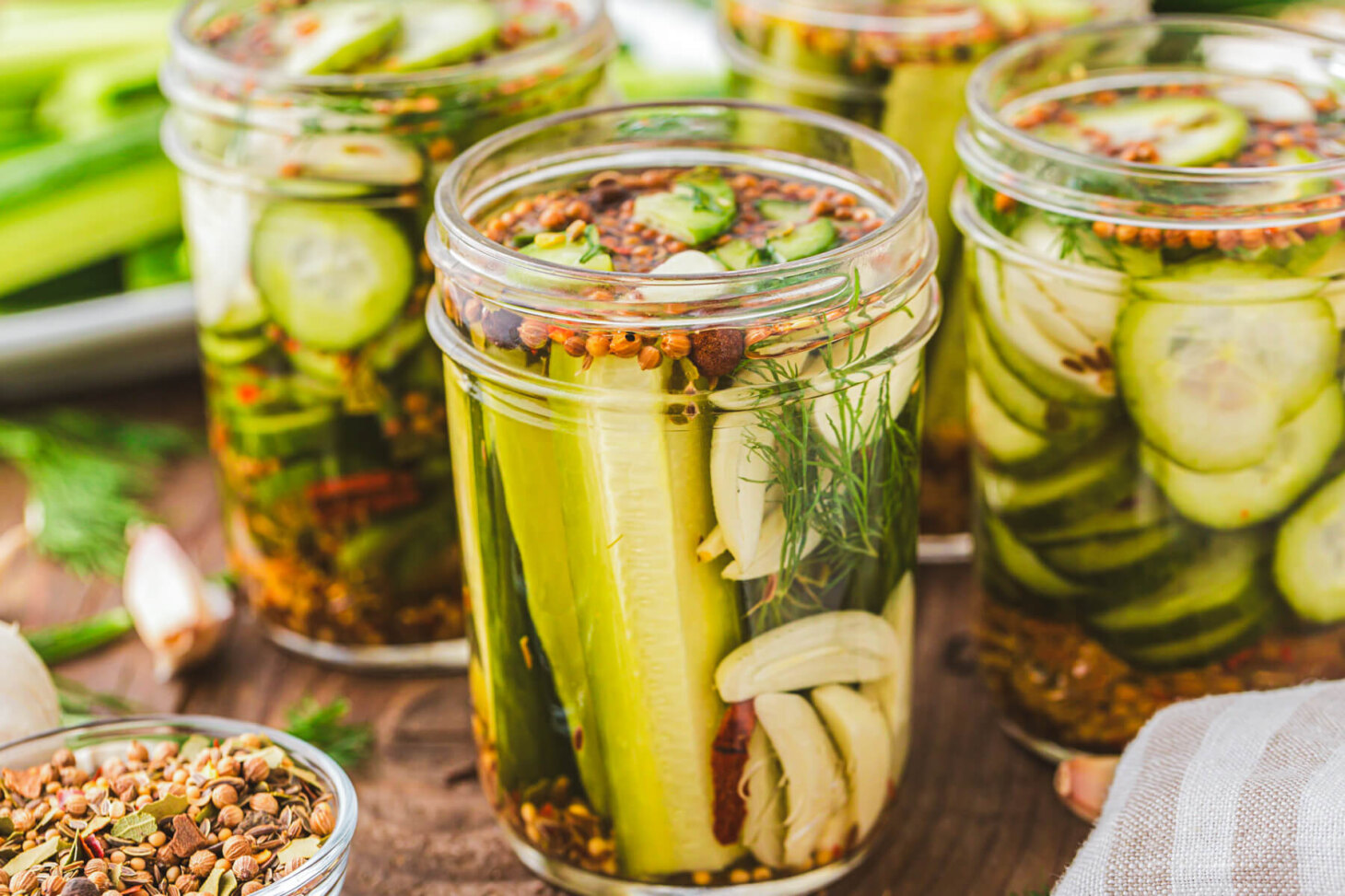 Four pint jars filled with refrigerator dill pickles, garlic cloves, dill, pickling spice and brine on a wooden platter.