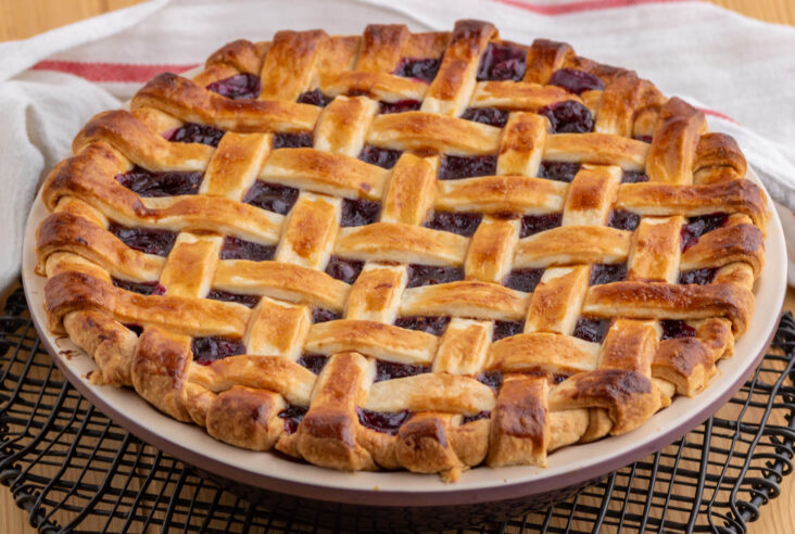 A golden baked fruit pie with a perfect lattice crust on a wooden table.