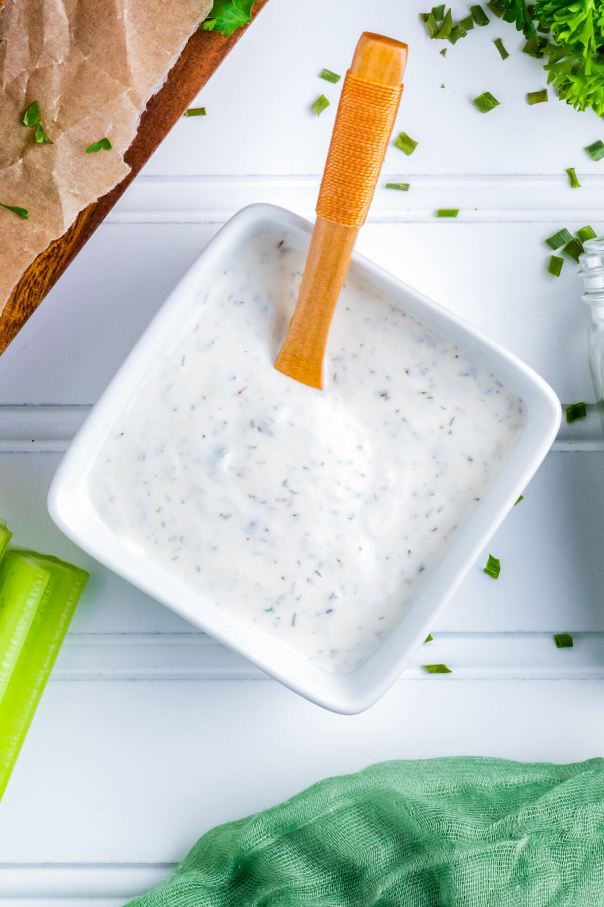 A small square white bowl filled with creamy homemade ranch dip and a small wooden spoon.
