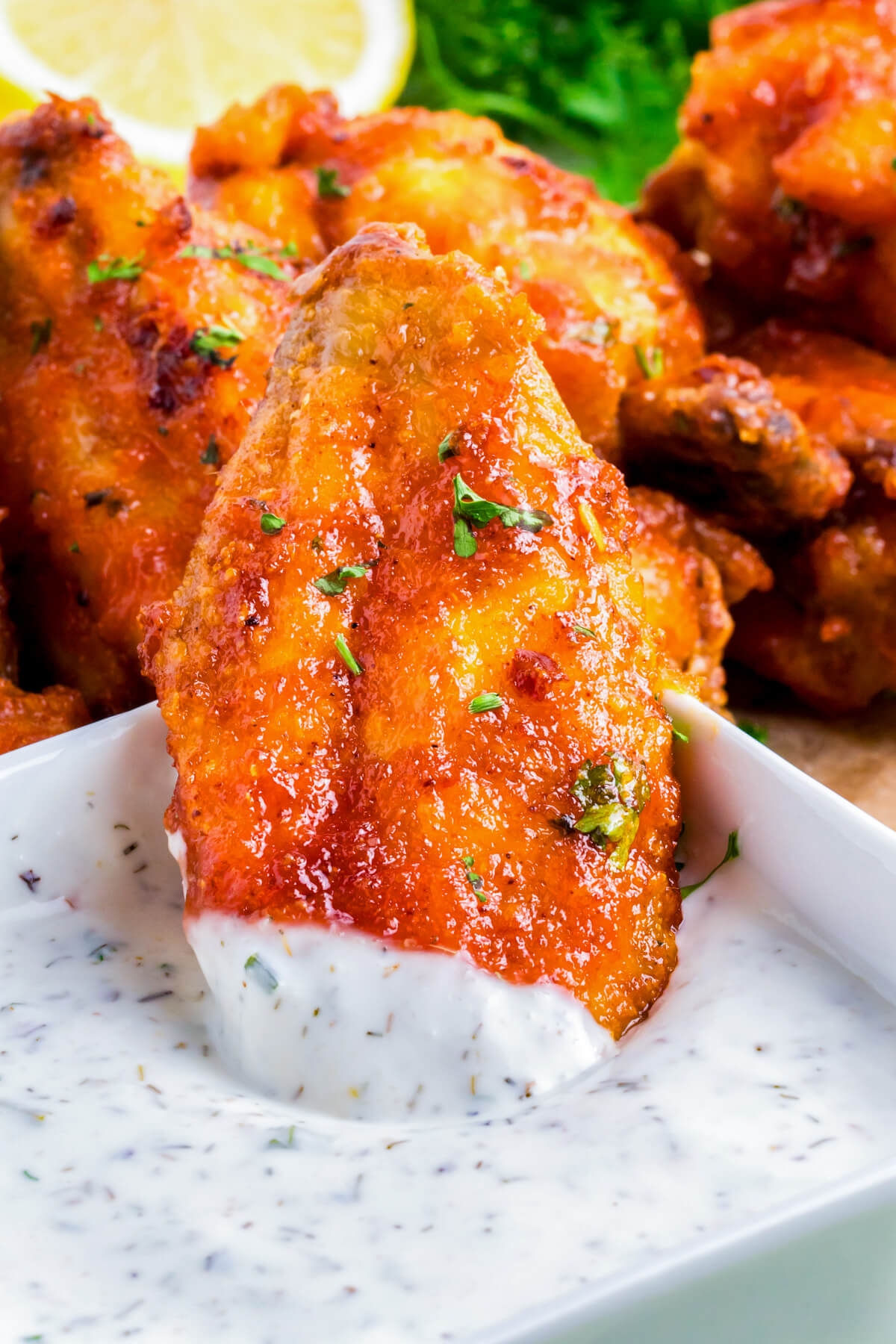 A vibrant orange Hot honey chicken wing being dipped into homemade ranch dressing.