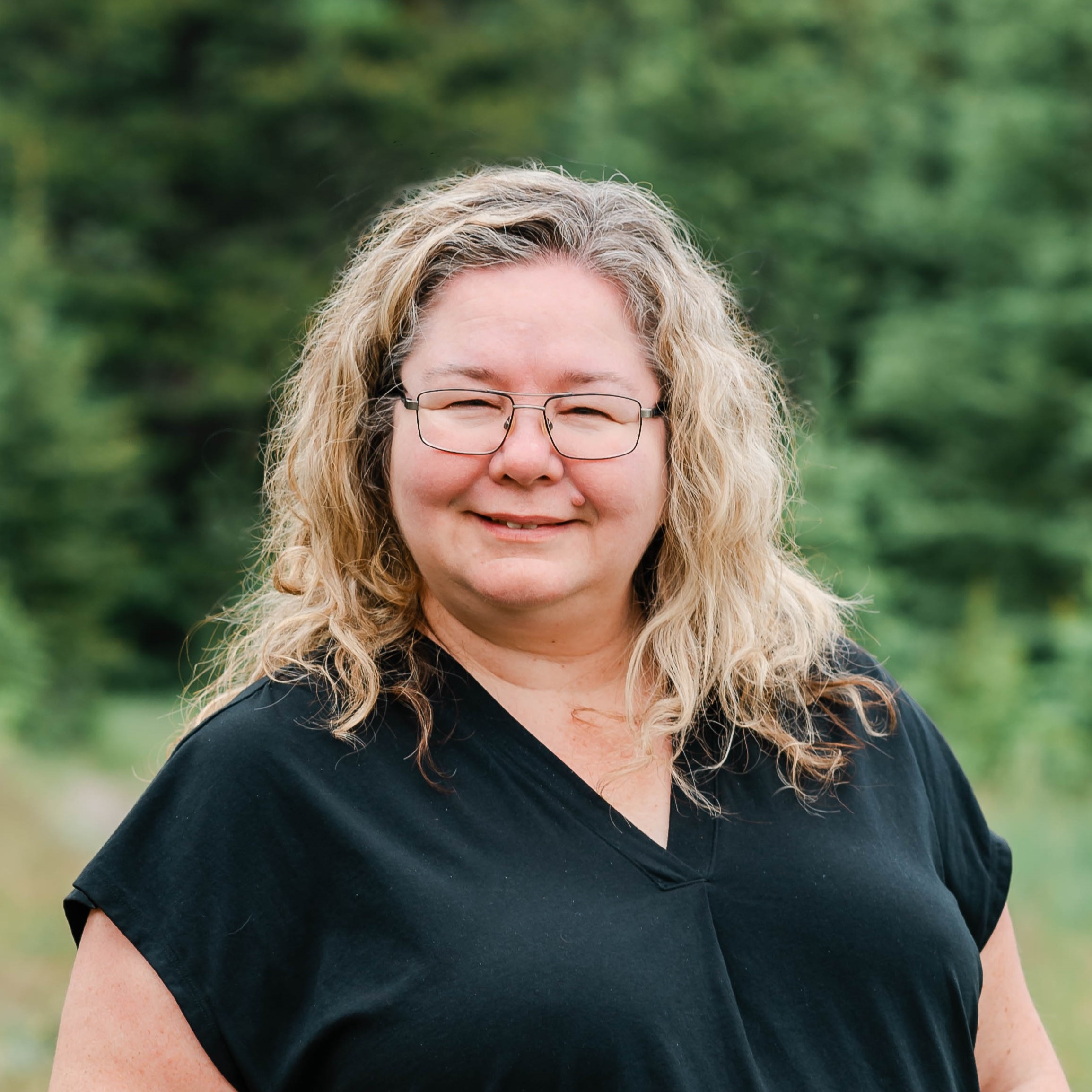 A portrait of Bernice Hill in front of spruce trees.