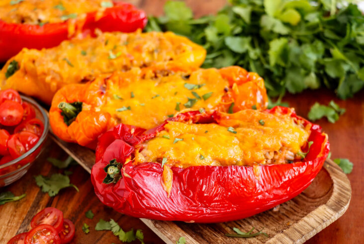 Three cheesy stuffed peppers on a wooden cutting board