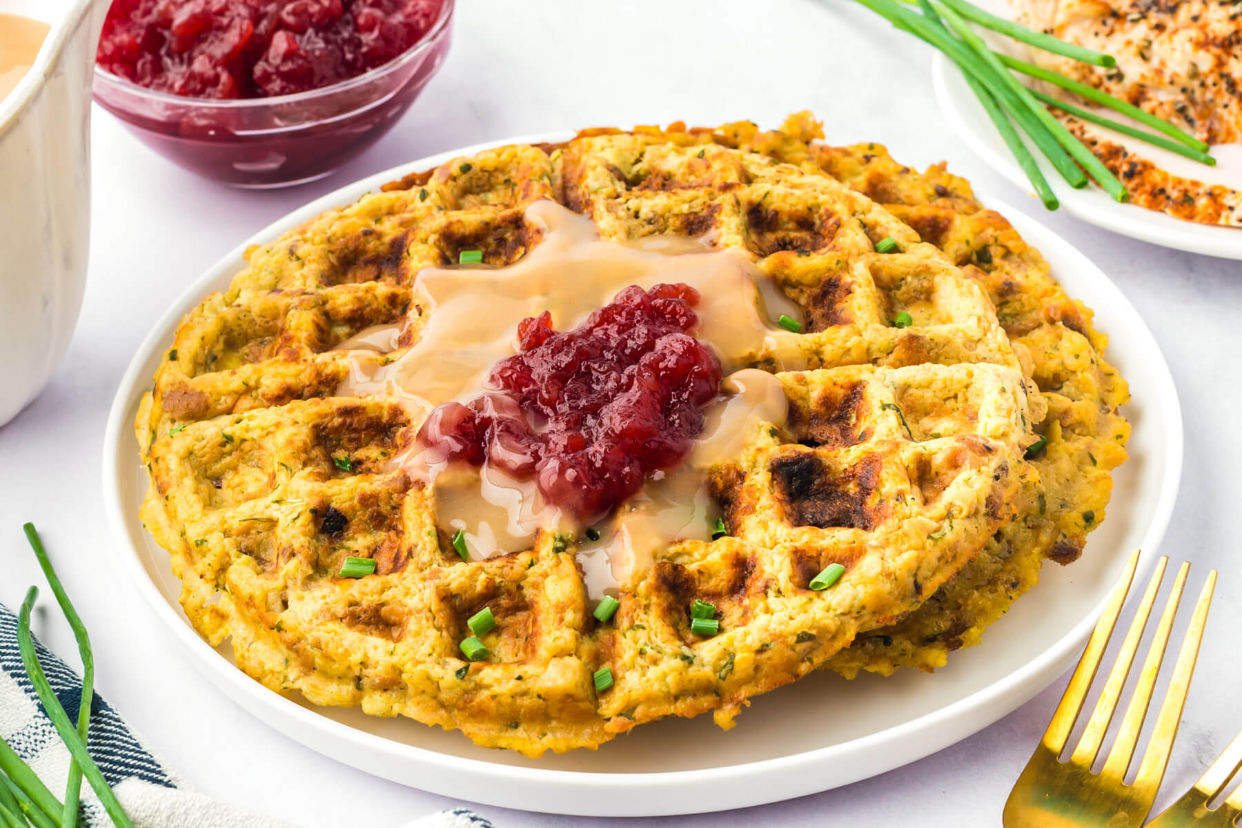 A white plate containing two crispy golden Stuffing Waffles topped with gravy and cranberry sauce.