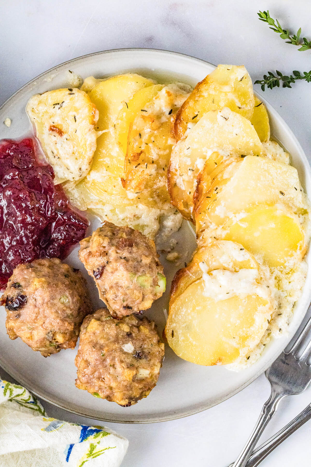 A dinner plate containing meatballs, cranberry sauce, and potatoes au gratin.