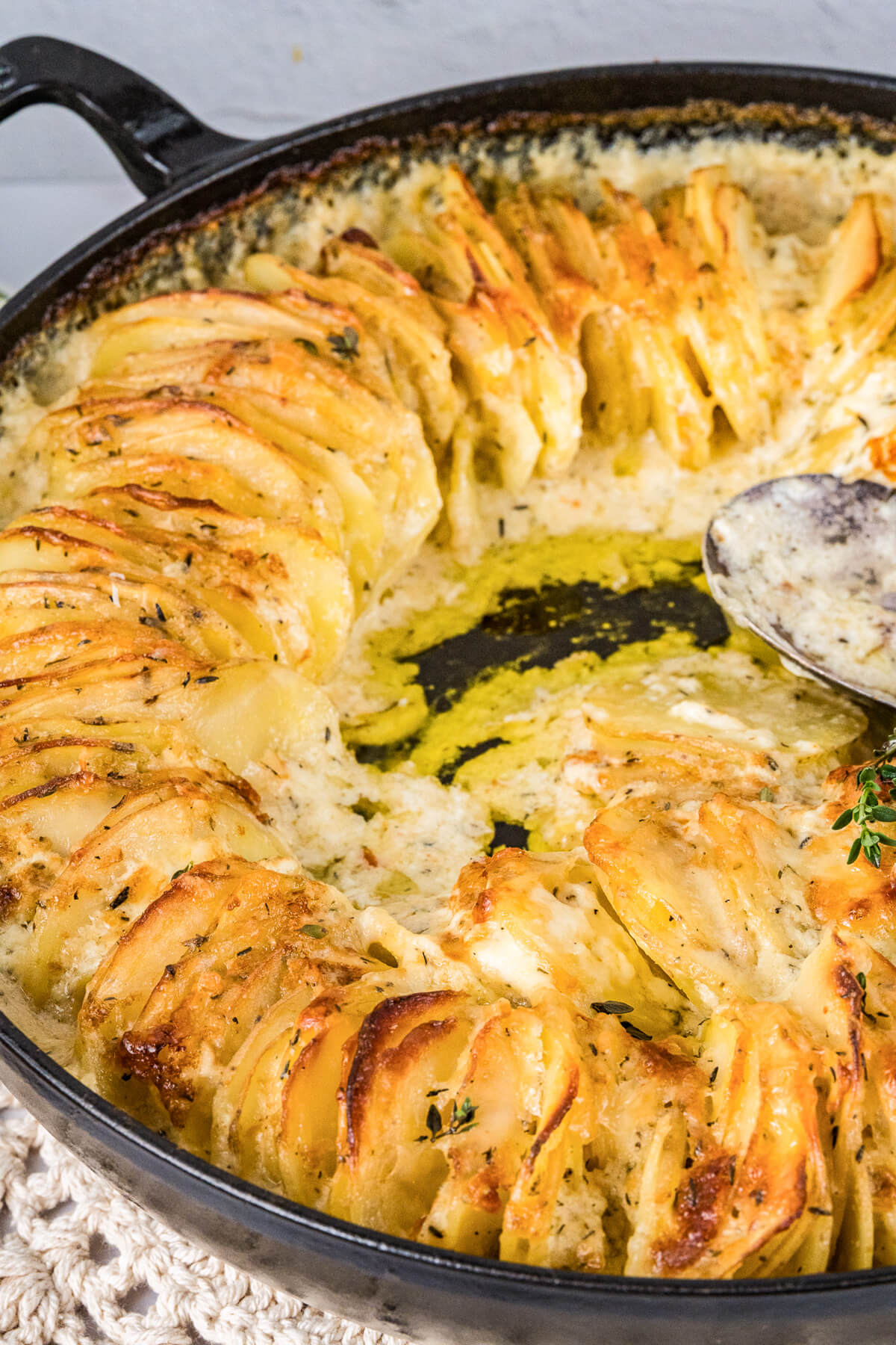 A large Staub baking dish containing golden baked cheesy potatoes au gratin and fresh thyme leaves.