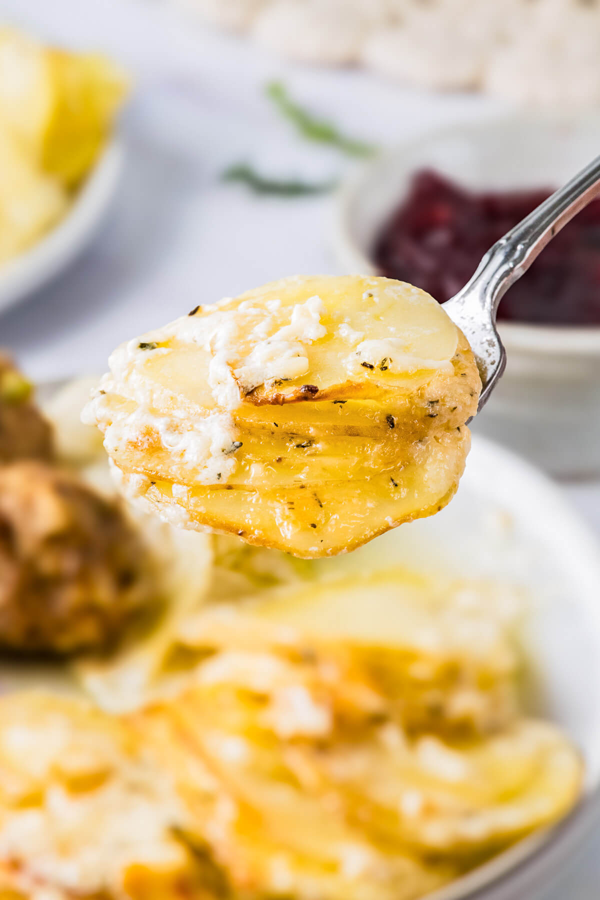 A spoon containing a serving of golden baked cheesy potatoes au gratin and fresh thyme leaves.