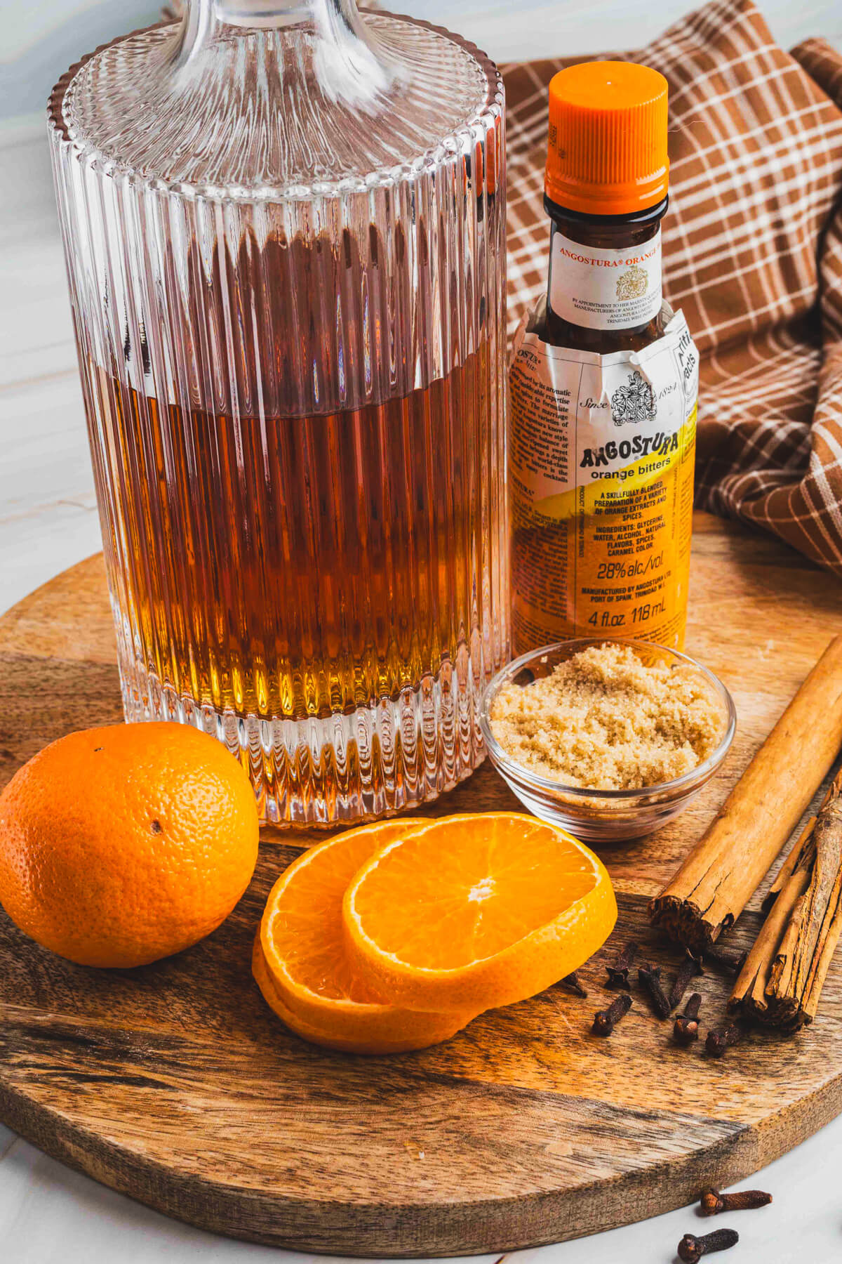 Ingredients required to make and garnish a bourbon old fashioned cocktail on a wooden board.