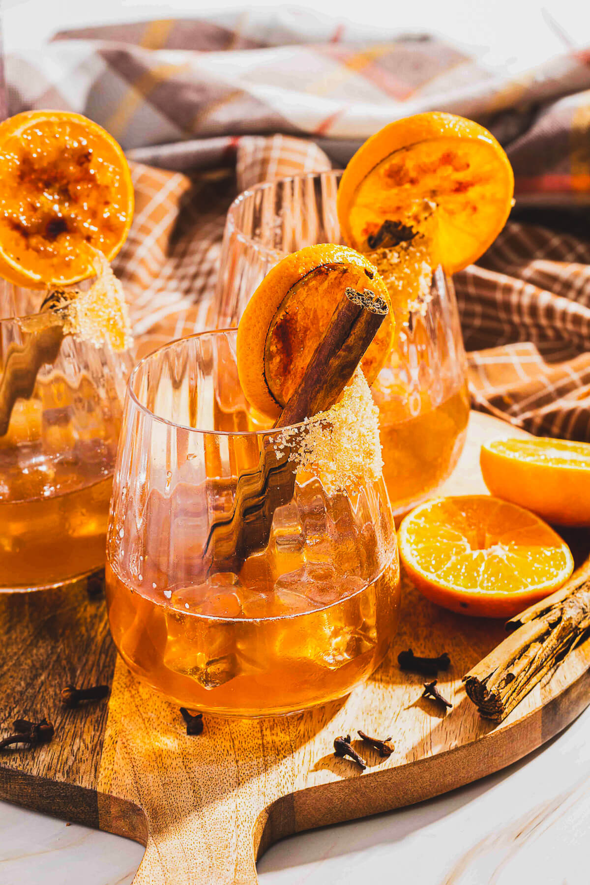 Three bourbon old fashioned cocktails in a rocks glasses garnished with orange slices and cinnamon sticks on a wooden board.