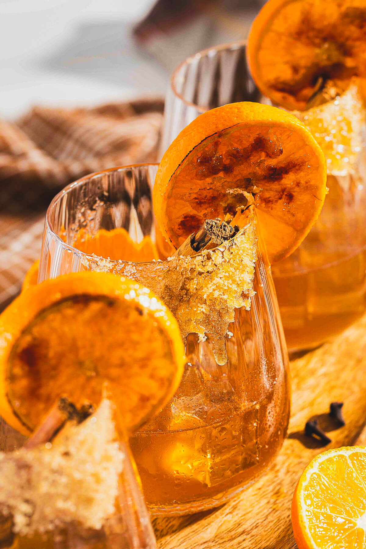 Three bourbon old fashioned cocktails in a rocks glasses garnished with orange slices and cinnamon sticks on a wooden board.