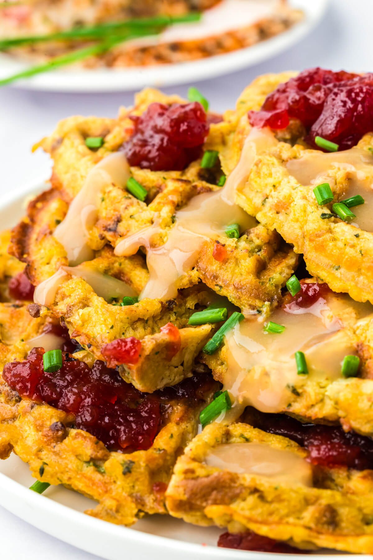 A plate stacked high with crispy golden Stuffing Waffles topped with gravy and cranberry sauce.