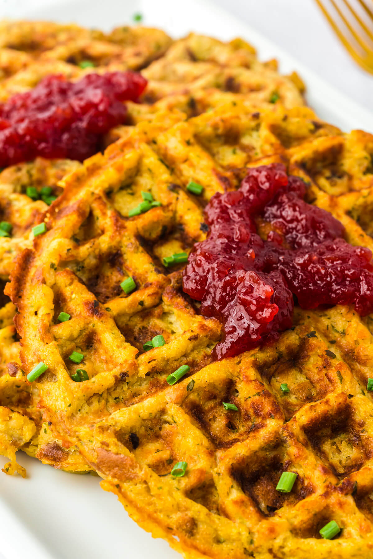 A long white platter containing two crispy golden Stuffing Waffles topped with cranberry sauce.