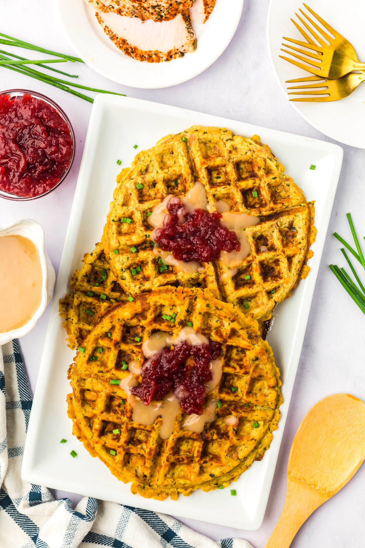 A long white platter containing two crispy golden Stuffing Waffles topped with gravy and cranberry sauce.