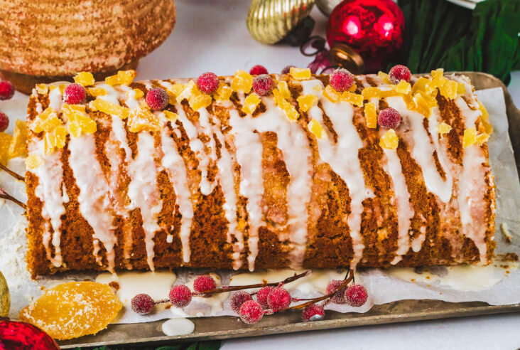 An entire decorated Gingerbread Swiss Roll Cake on a platter in front of holiday decorations.