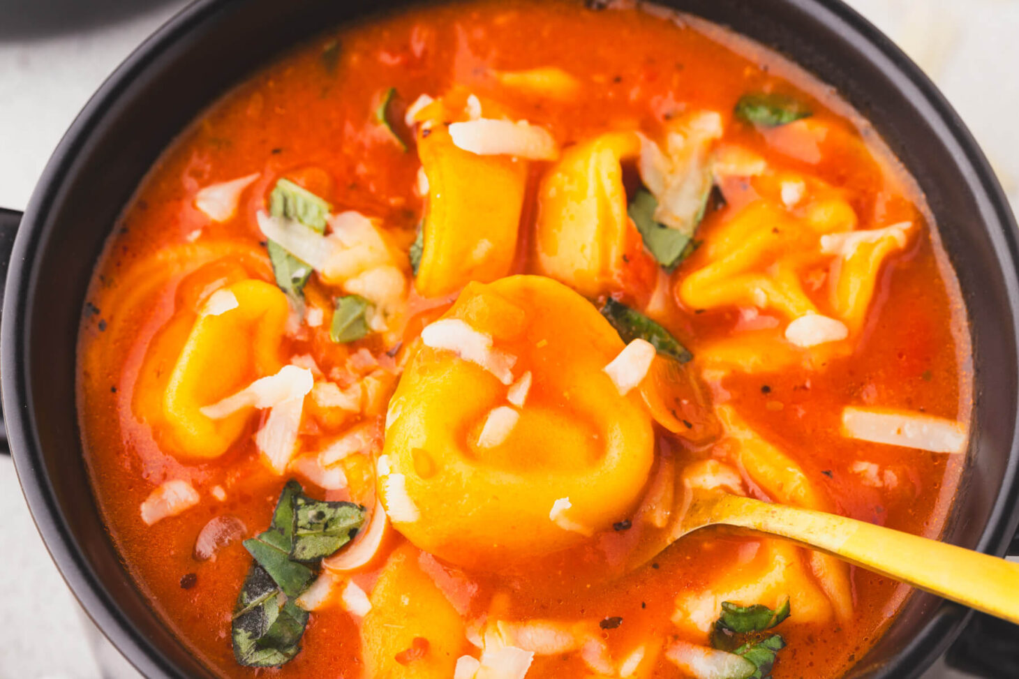 Close up images of cooked tortellini in a bowl of creamy cheesy tomato soup.