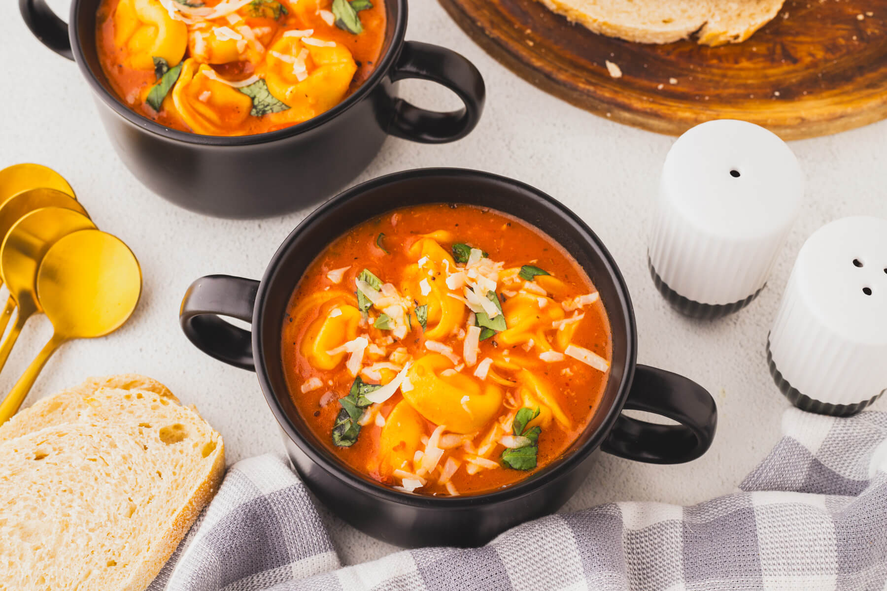 Two black soup bowls with handles filled with creamy cheesy tomato tortellini soup.