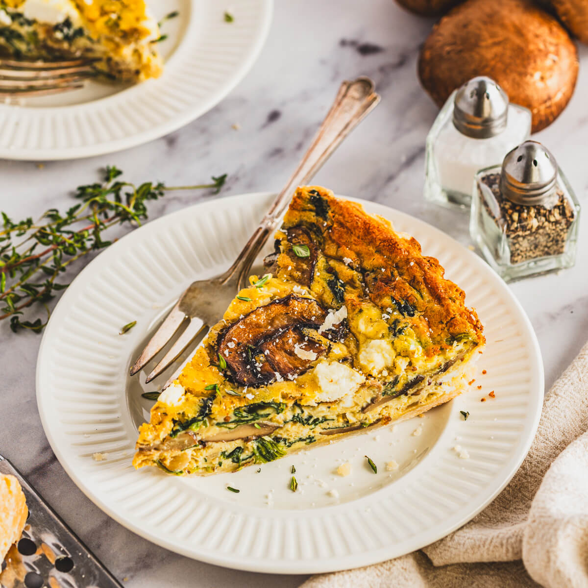 A slice of Spinach Mushroom Quiche in a golden baked crust on a white plate.