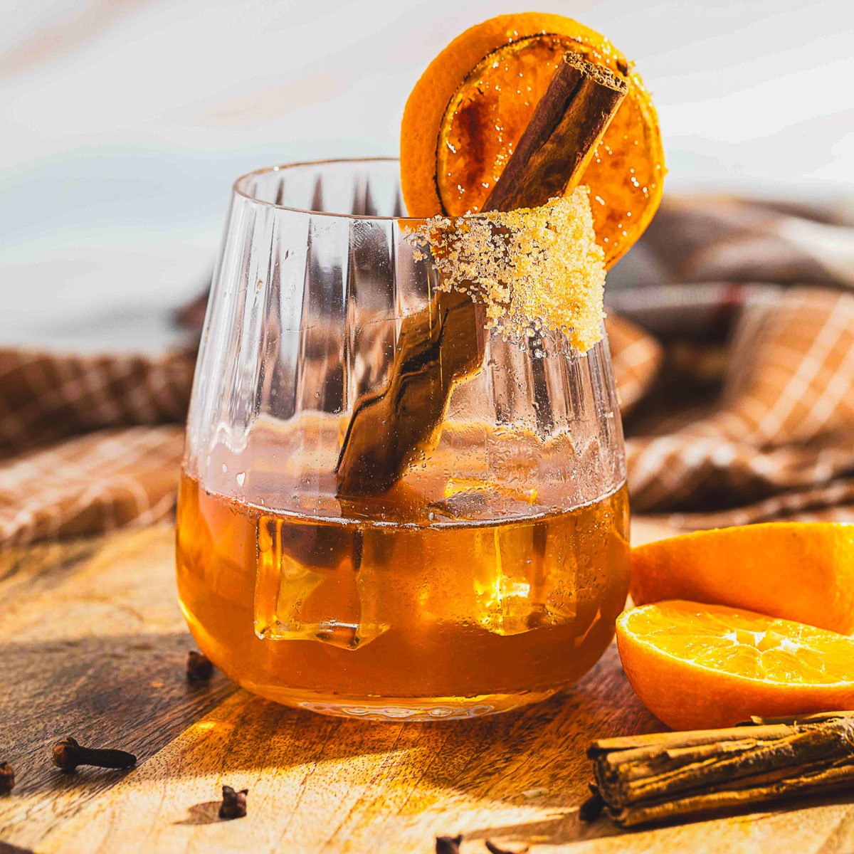 One bourbon old fashioned cocktail in a rocks glass garnished with an orange slice and cinnamon stick on a wooden board.