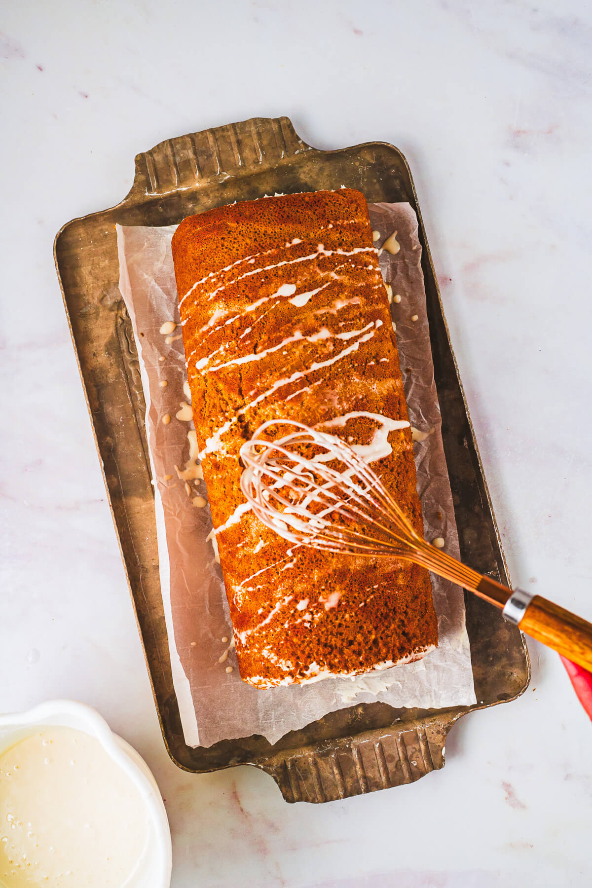 How to use a whisk to apply maple glaze to a gingerbread Swiss cake roll.