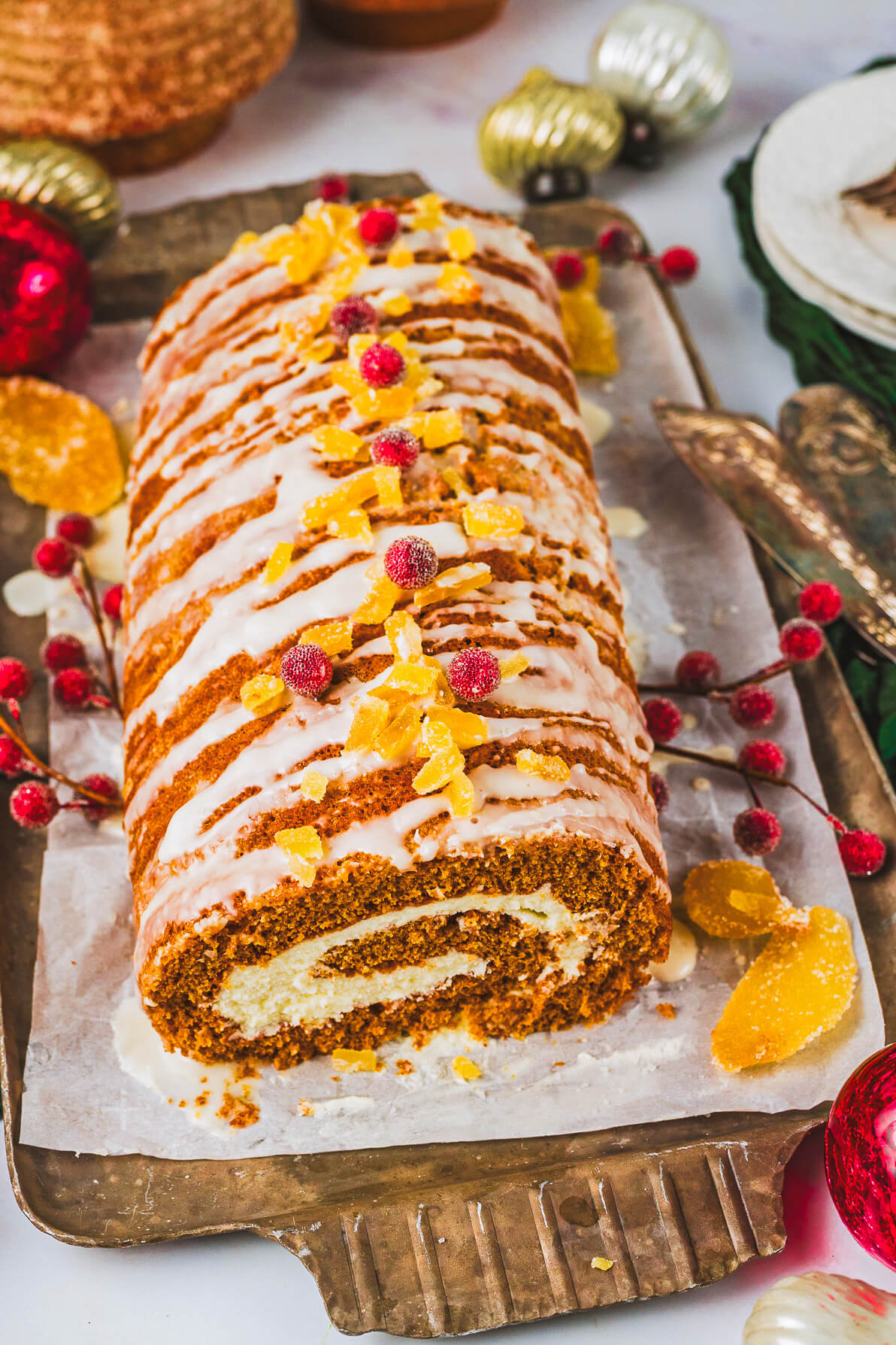 An entire decorated Gingerbread Swiss Roll Cake on a wooden platter surrounded by holiday decorations.