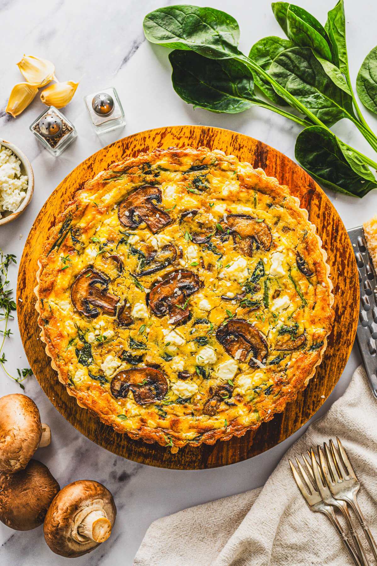 A whole Spinach Mushroom Quiche in a golden baked crust on a round wooden serving board.