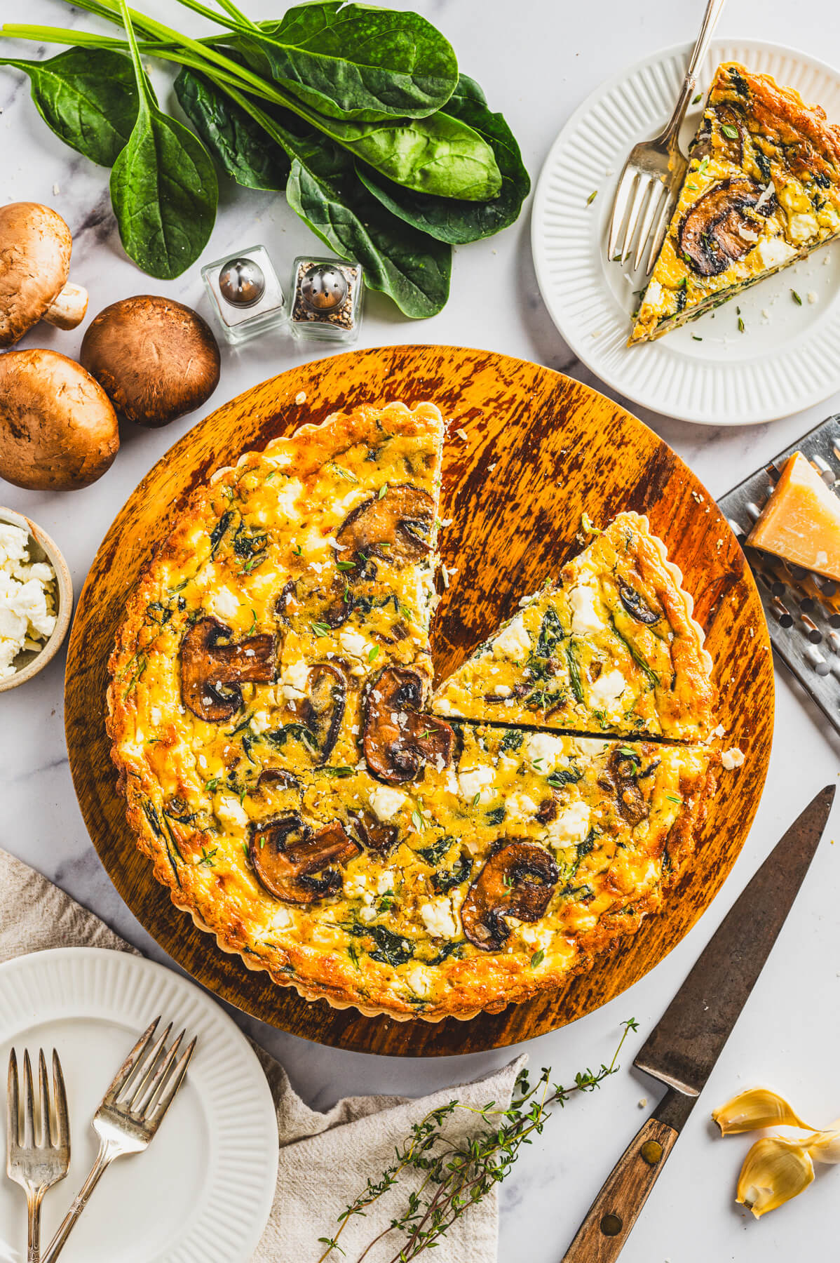 A Spinach Mushroom Quiche in a golden baked crust on a round wooden serving board with one slice missing.