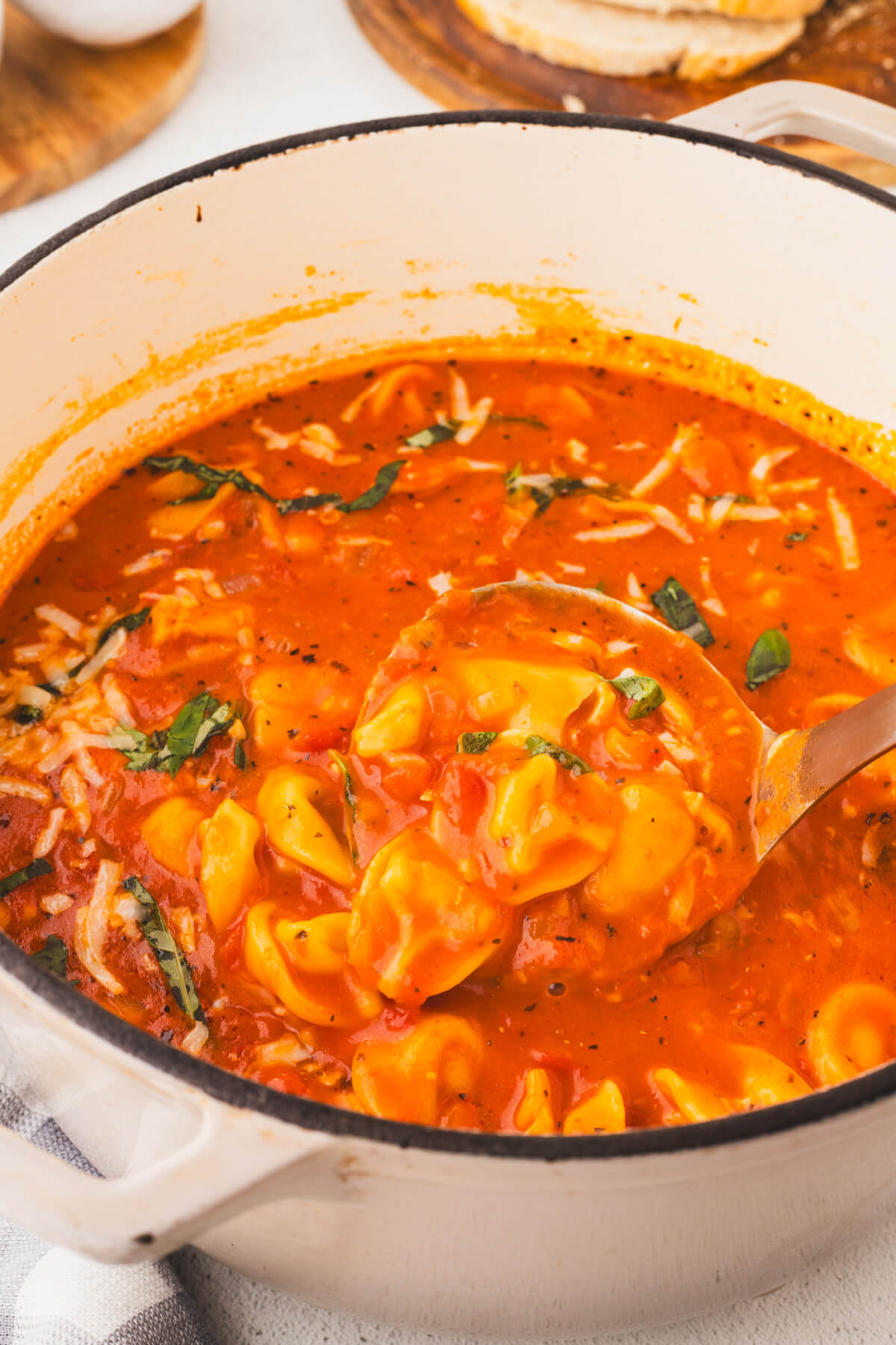 A white Dutch oven filled with creamy cheesy tomato tortellini soup.