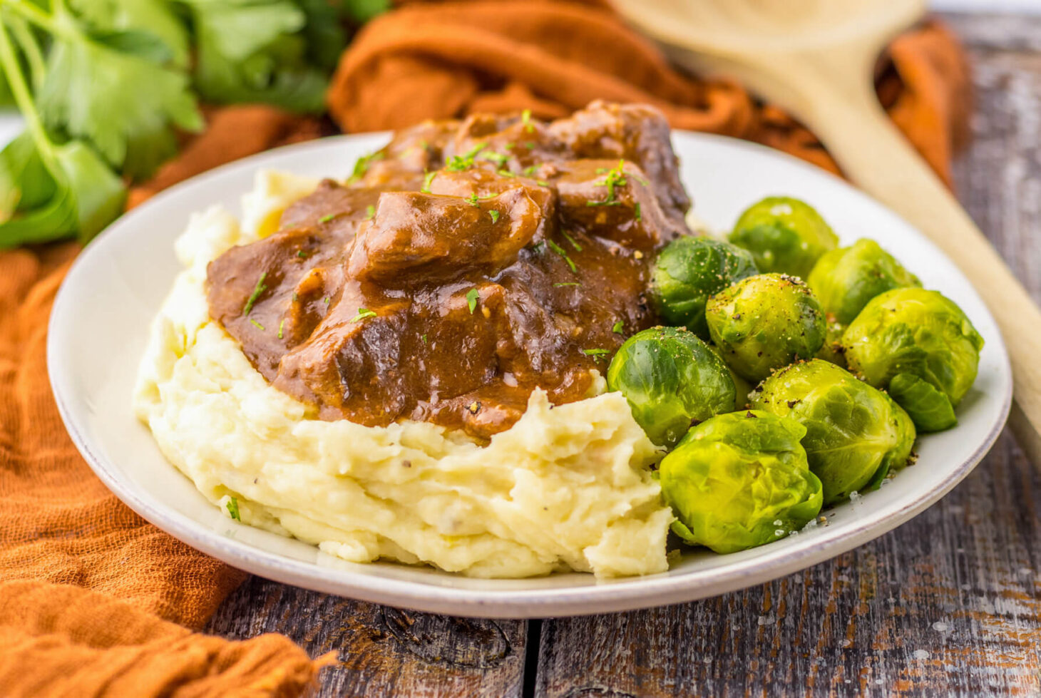 Tender slow cooked beef tips in a rich and flavourful gravy on a bed of mashed potatoes beside Brussels sprouts.