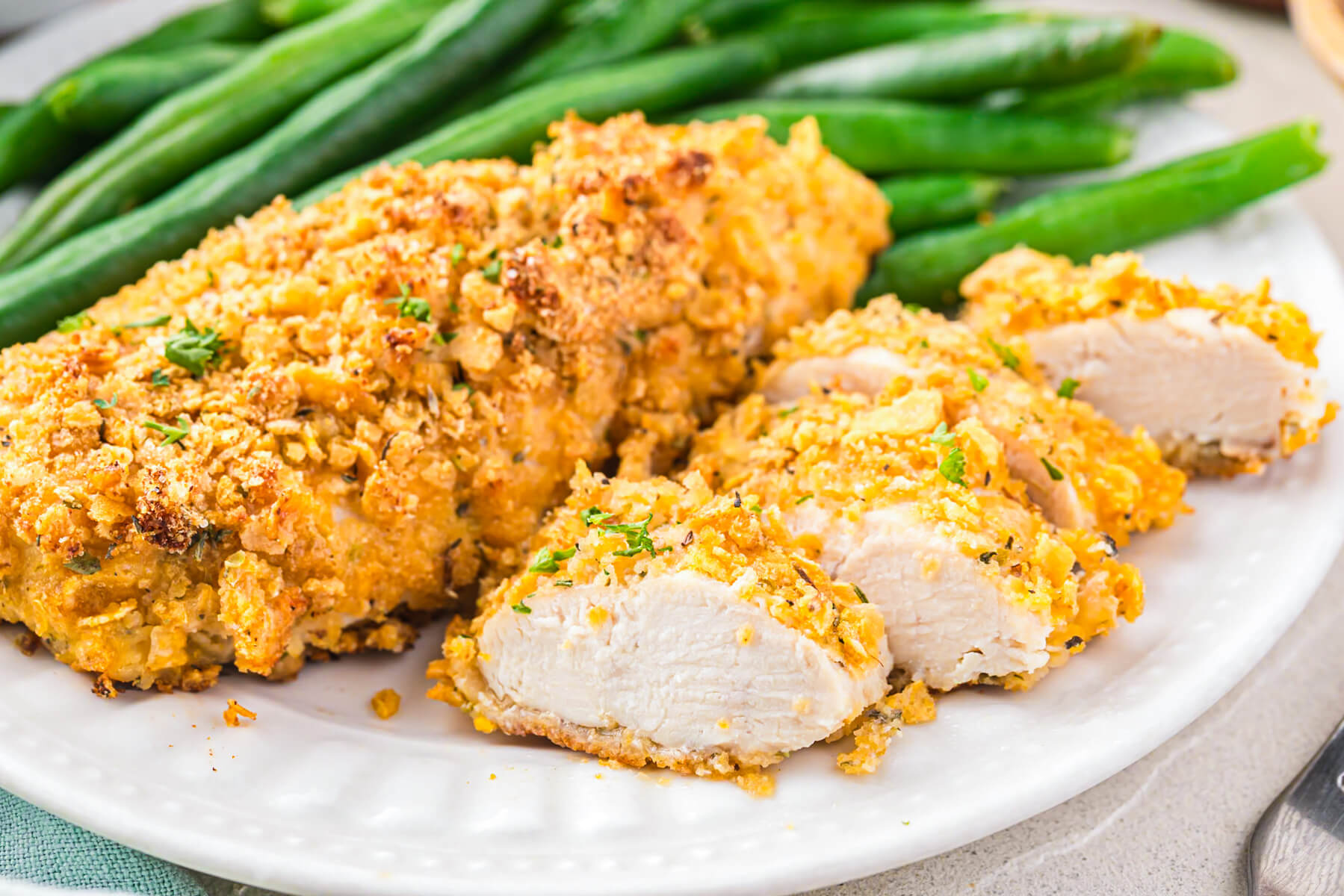 A white plate containing two golden cornflake chicken tenders and a side of steamed green beans.