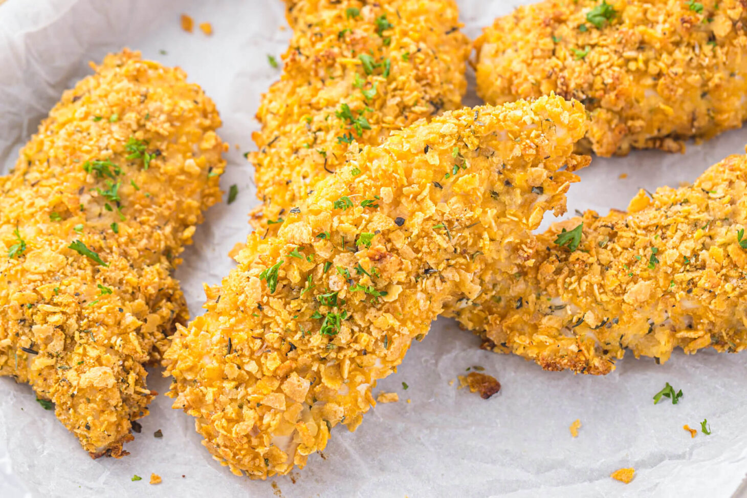 A parchment lined baking tray containing six golden baked cornflake chicken tenders.