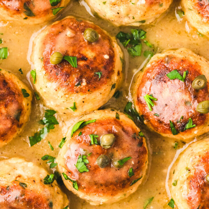 Three chicken meatballs in a bright yellow piccata sauce garnished with chopped Italian parsley.