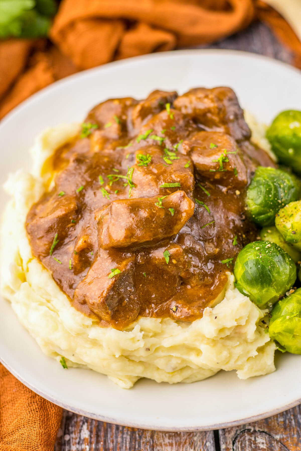 Tender slow cooked beef tips in a rich and flavourful gravy on a bed of mashed potatoes beside Brussels sprouts.