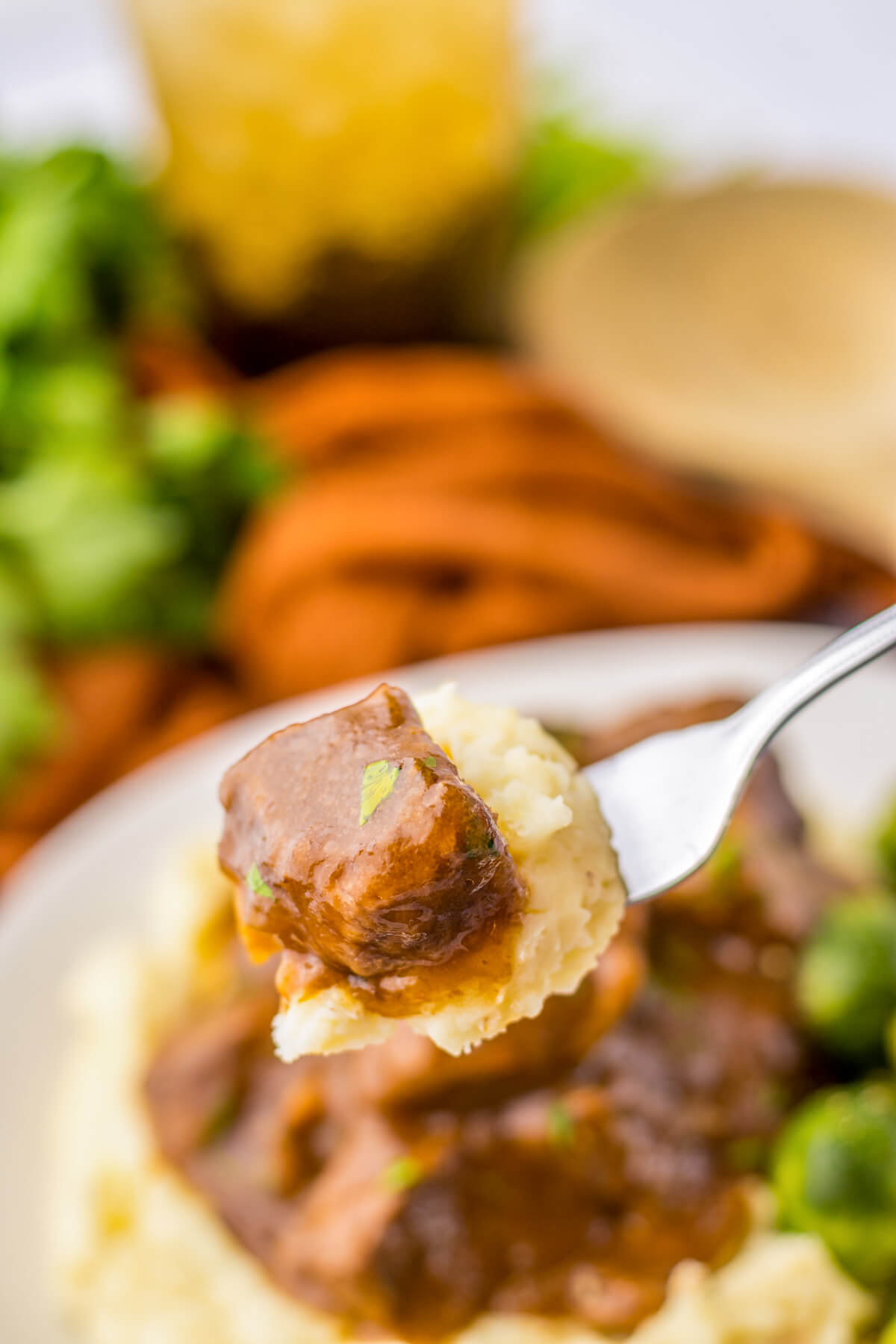 A forkful of mashed potatoes topped with a beef tip and gravy over a dinner plate.