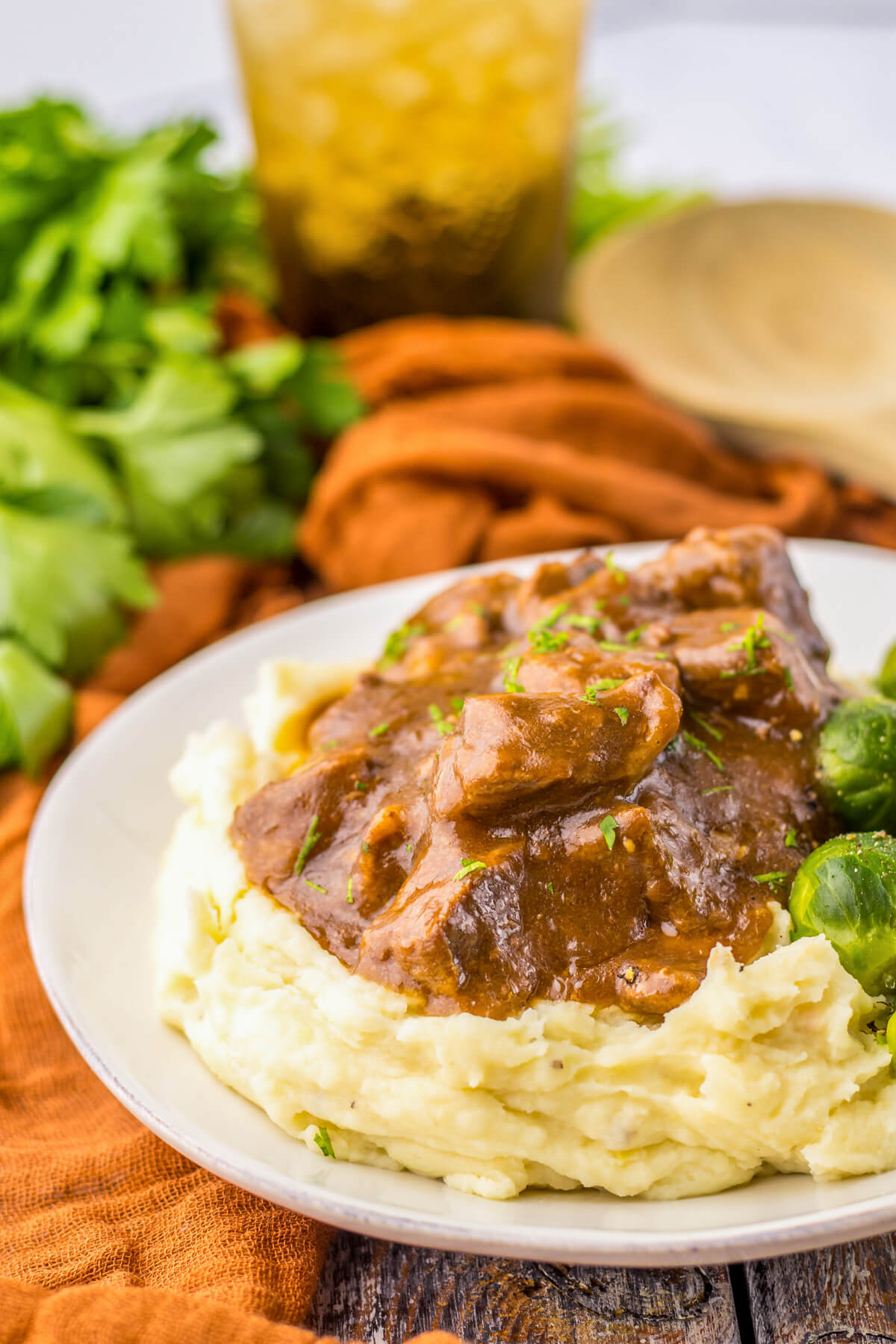 Tender slow cooked beef tips in a rich and flavourful gravy on a bed of mashed potatoes beside Brussels sprouts.