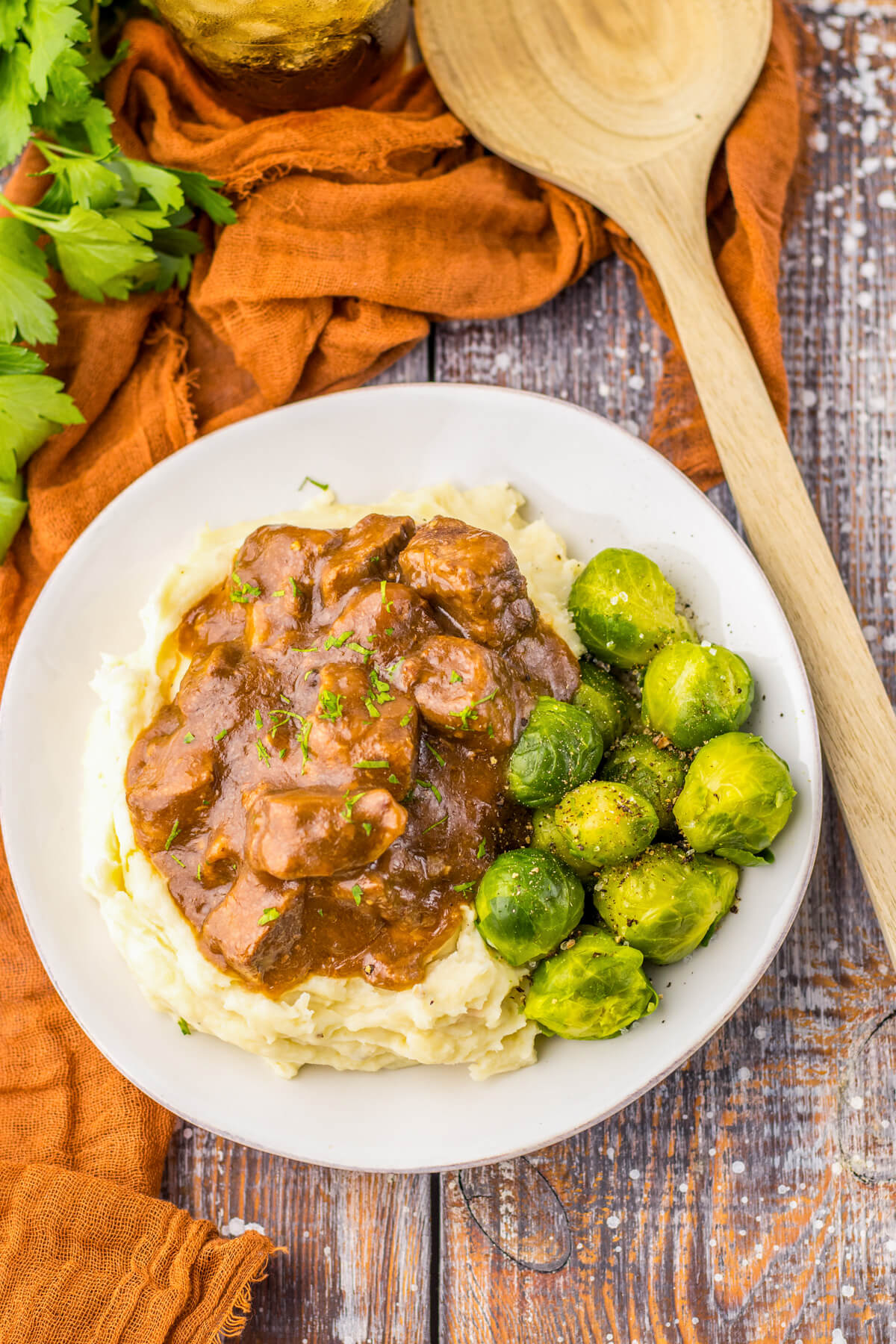 Tender slow cooked beef tips in a rich and flavourful gravy on a bed of mashed potatoes beside Brussels sprouts.